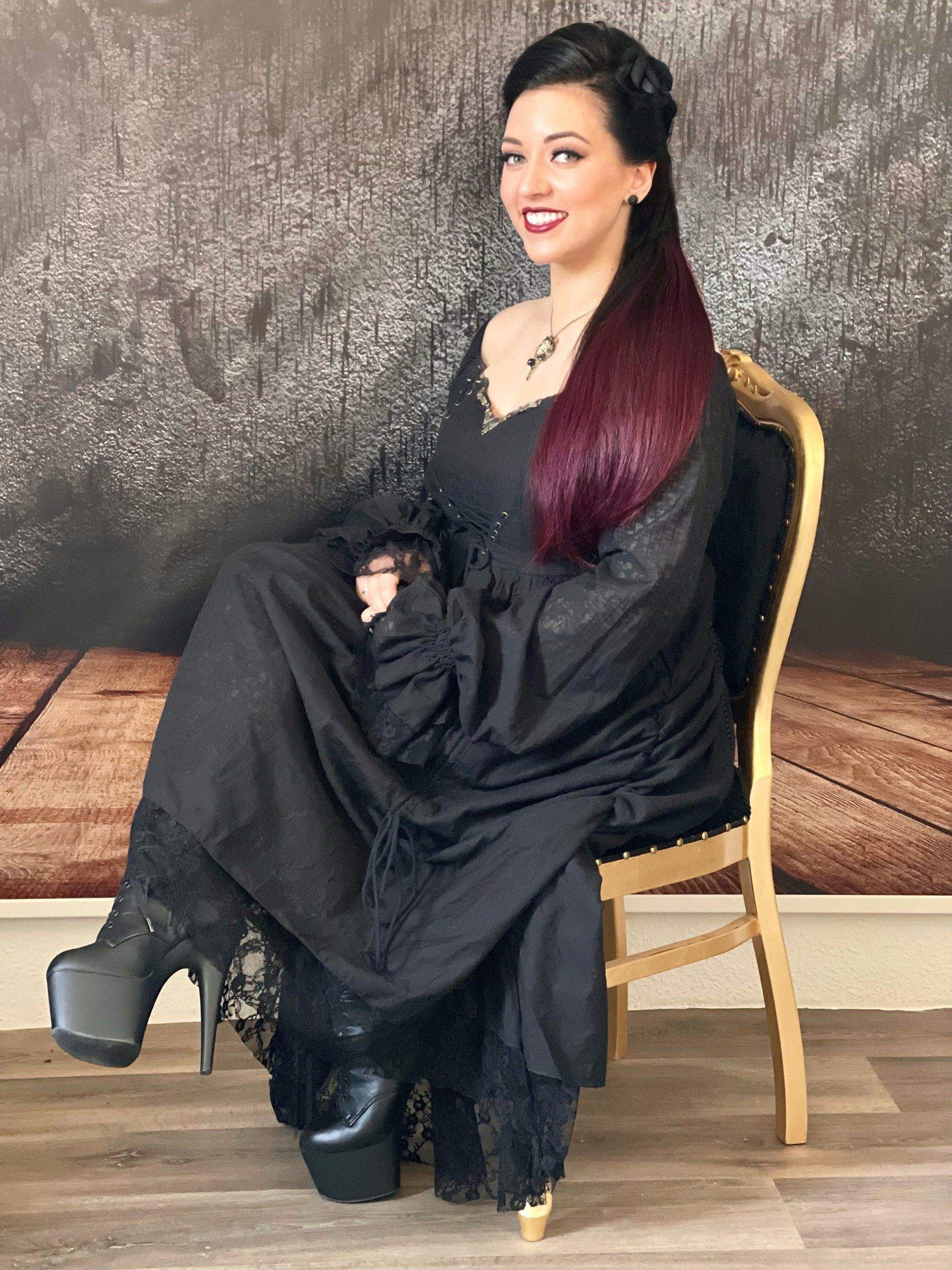 Eine Frau in einem schwarzen Kleid sitzt auf einem Stuhl.