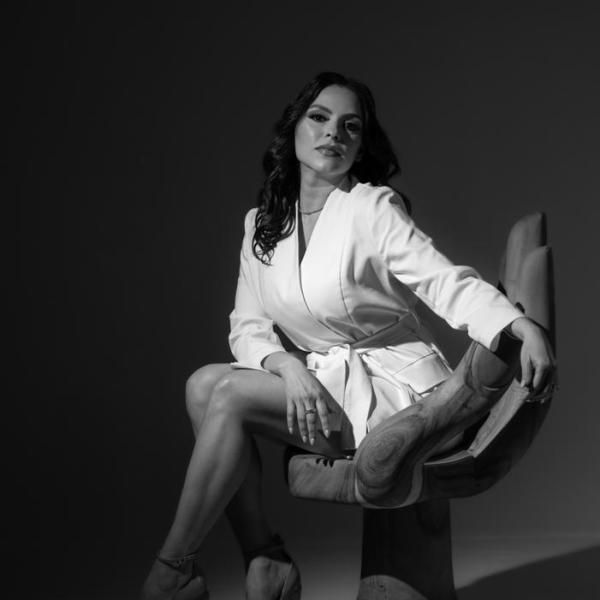 A woman in a white jacket is sitting in a chair with her legs crossed.