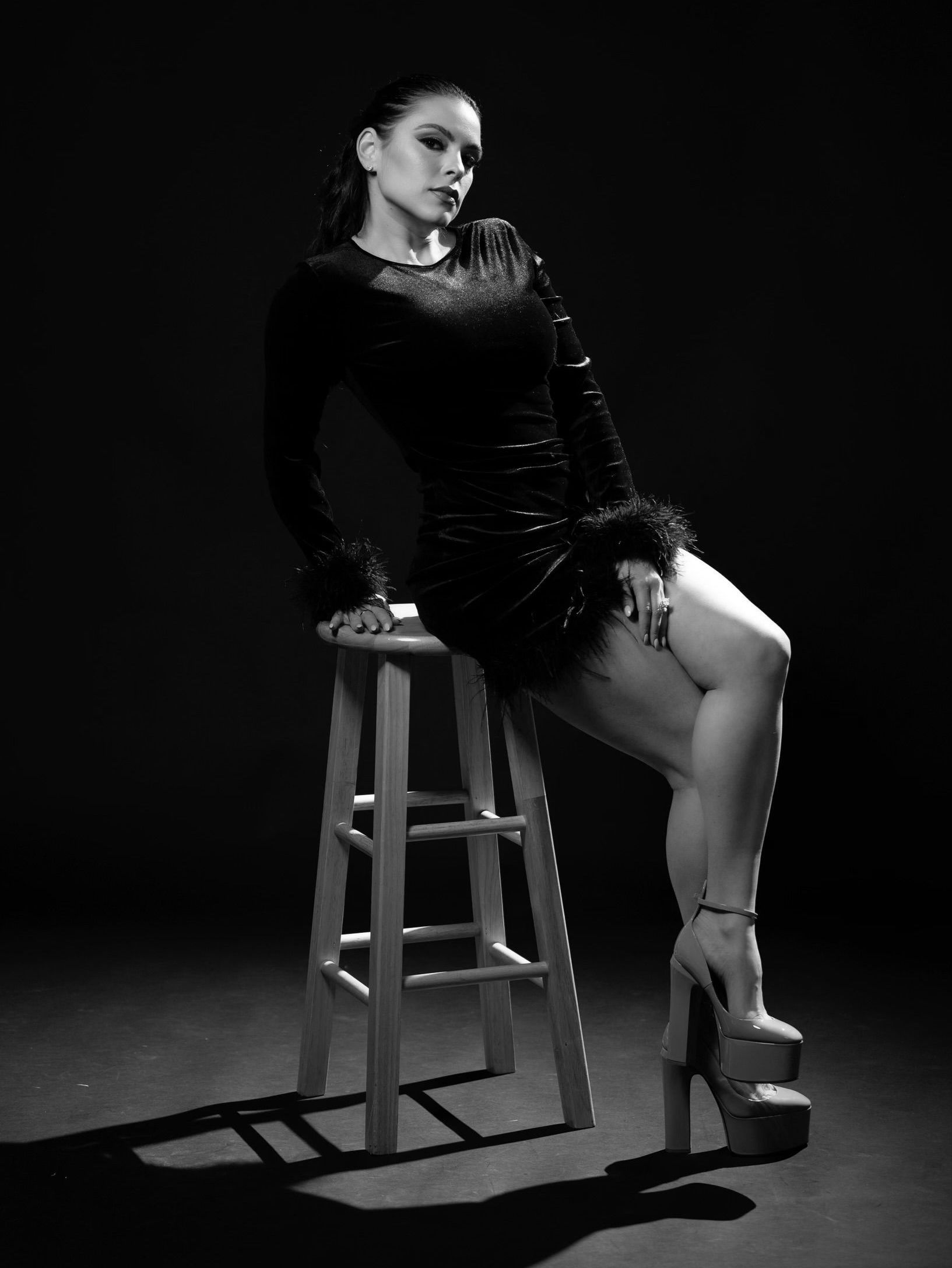 A woman in a black dress is sitting on a wooden stool.