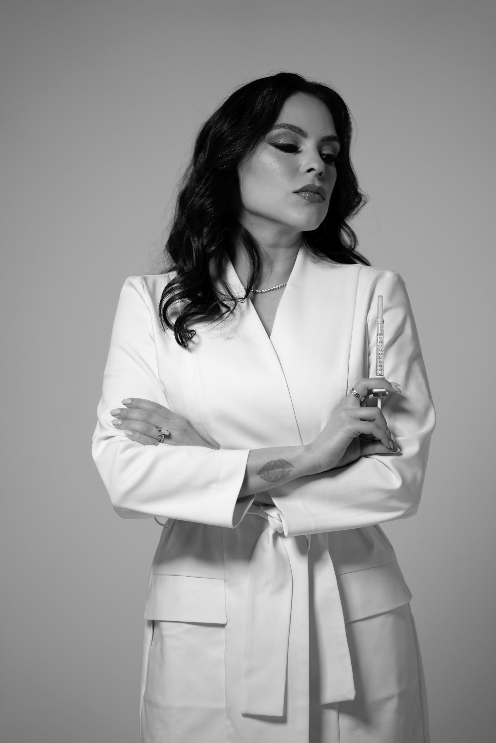 A woman in a white suit is standing with her arms crossed.