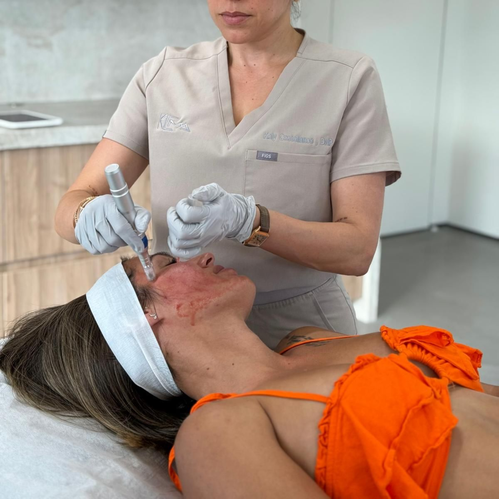A practitioner in medical scrubs uses a handheld microneedling device on a client's face in a clinical setting.