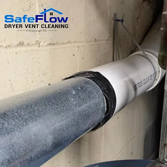 A white pipe is attached to a brick wall by safeflow dryer vent cleaning