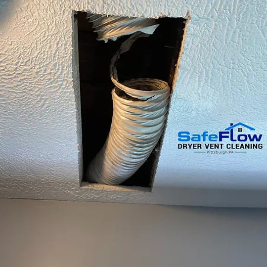 A white dryer vent hose is coming out of a hole in the ceiling.