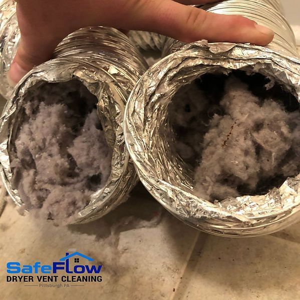 A person is holding two dryer vents filled with dust.