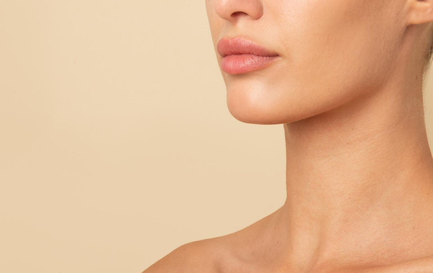 Close-up of a person's lower face, neck, and shoulder against a neutral, beige background.