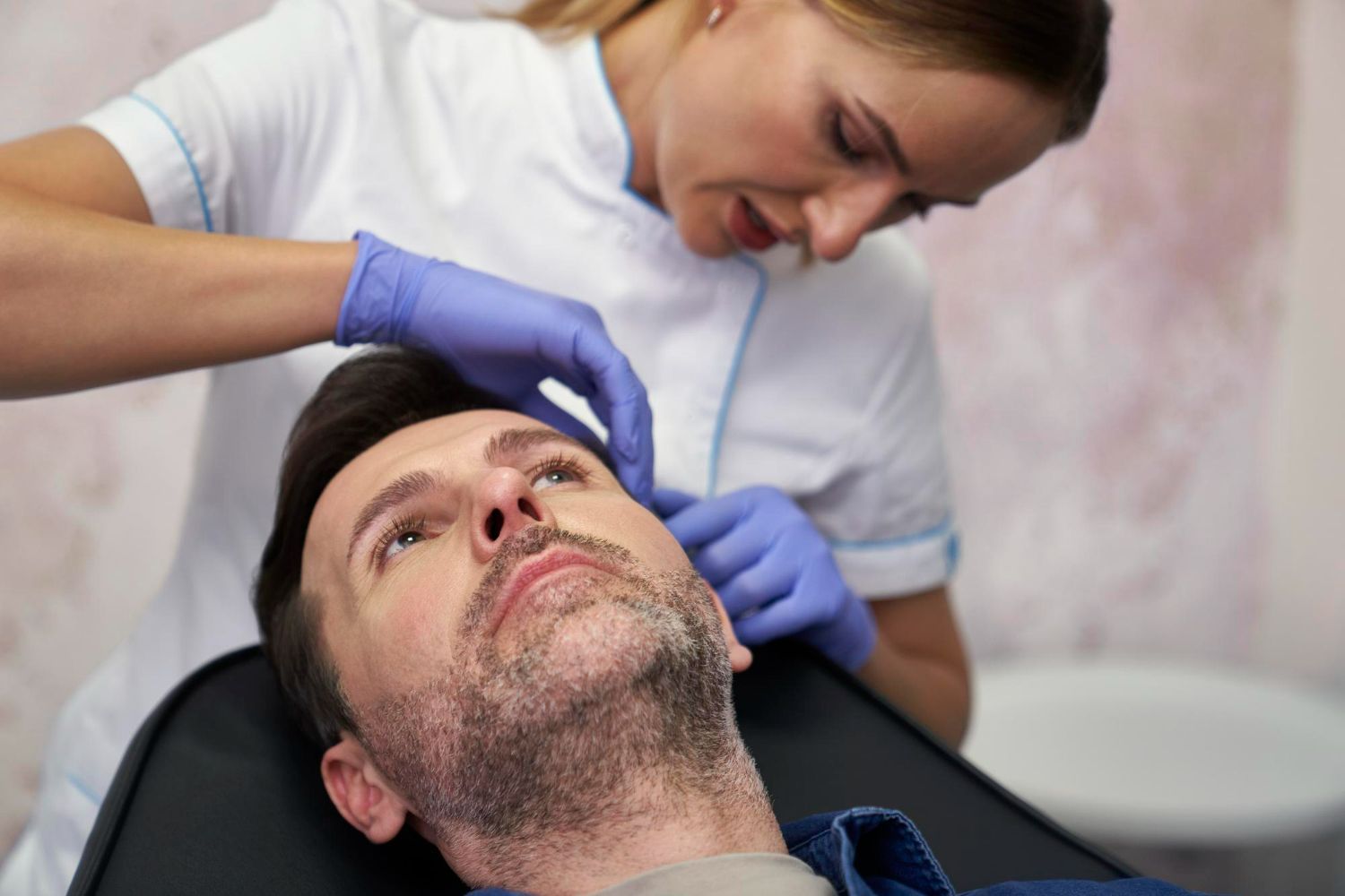 A professional wearing gloves prepares to perform a cosmetic procedure on a client's face in a clinical setting.