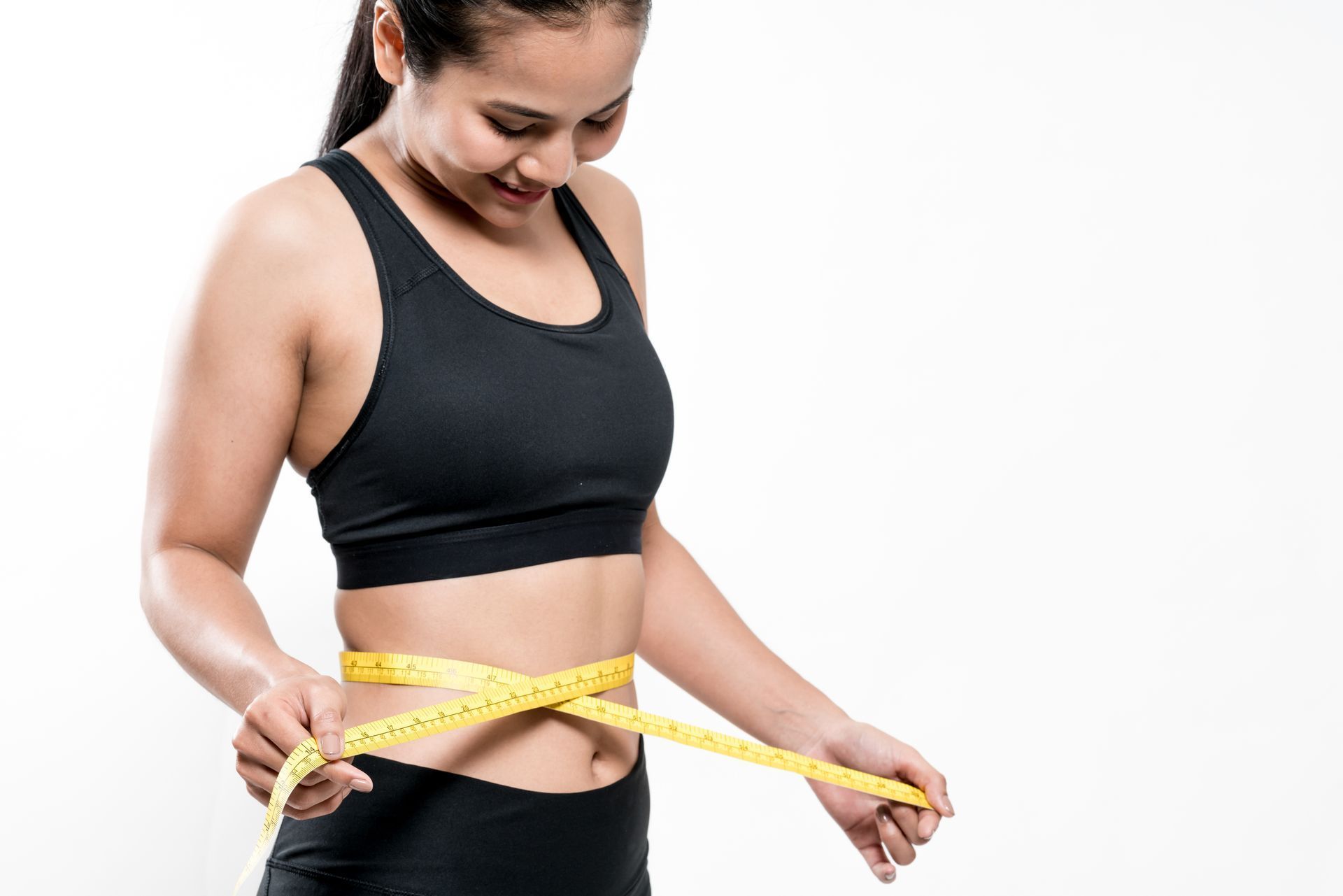 A woman is measuring her waist with a tape measure.