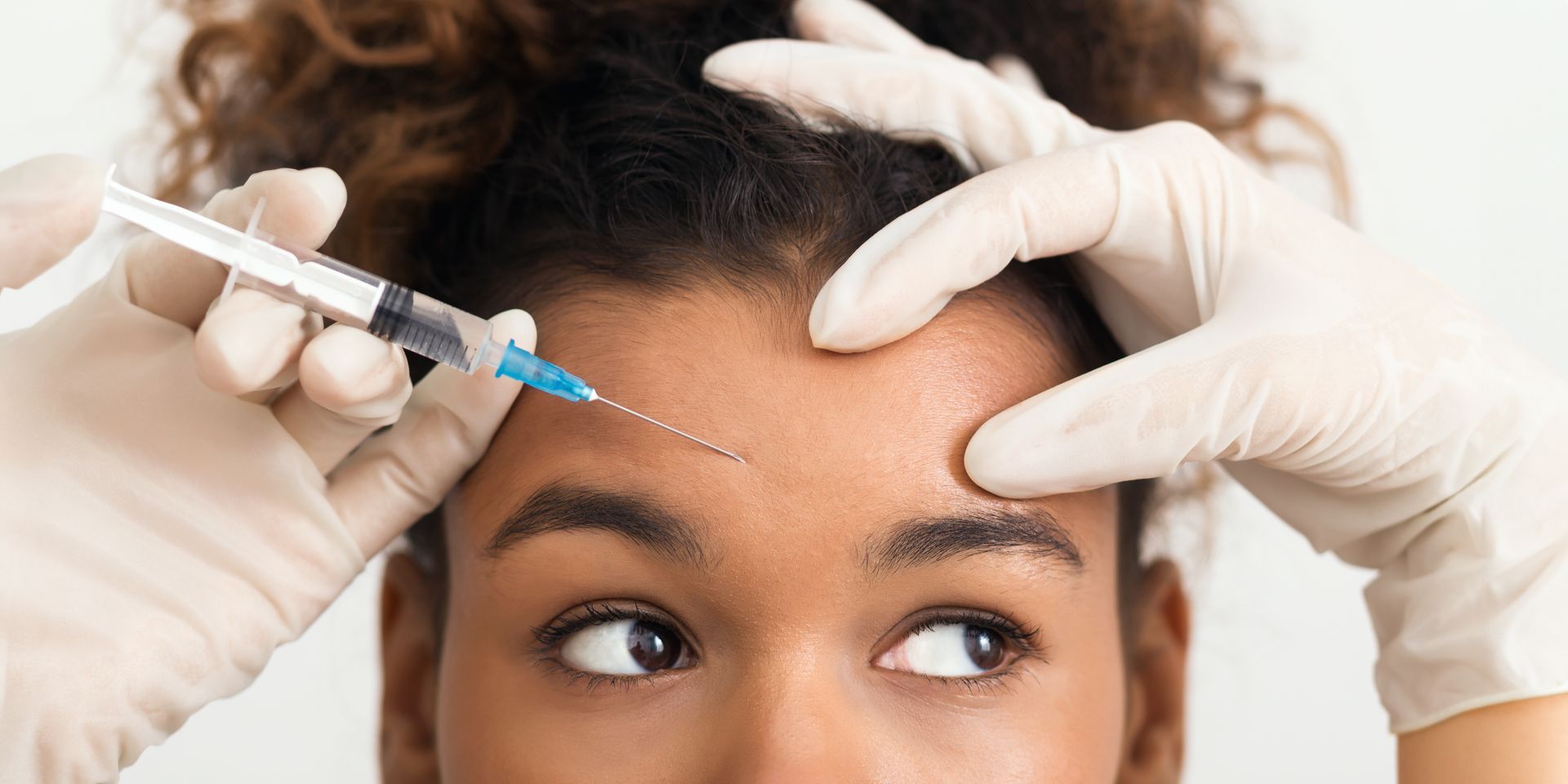 A person receiving an injection in their forehead. Gloved hands hold the person's face while injecting.