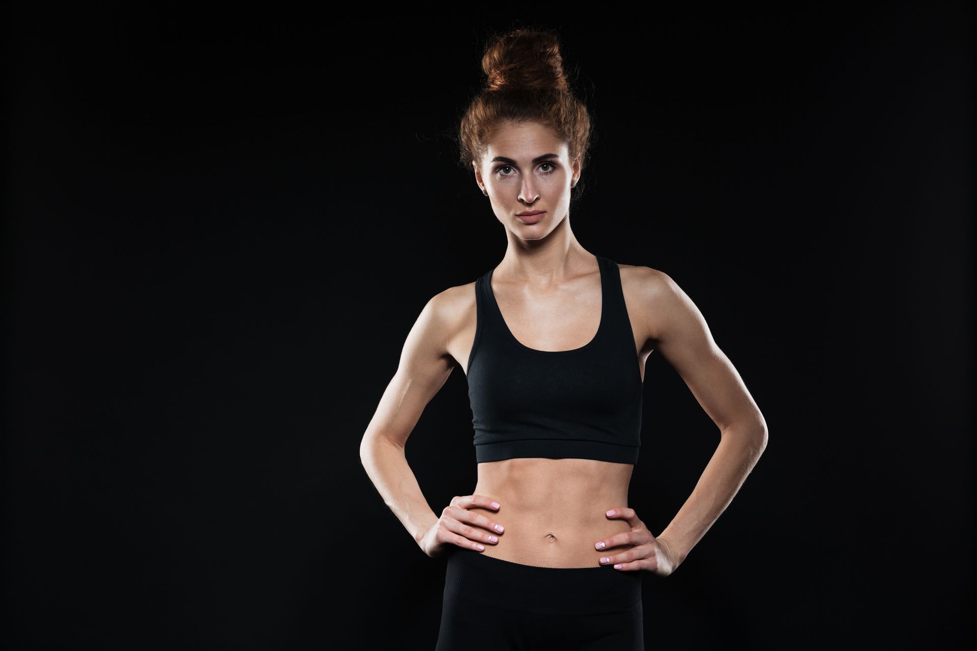a woman in a black sports bra is standing with her hands on her hips on a black background .