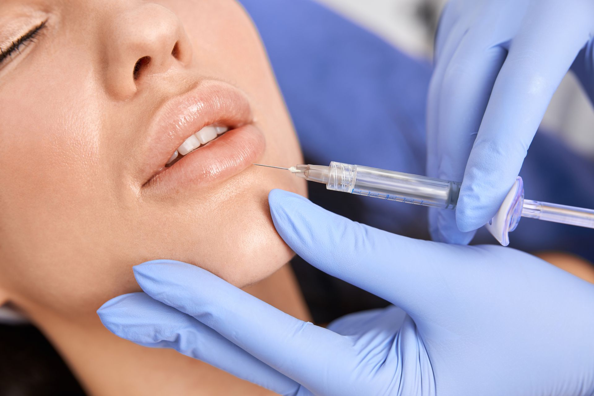 Lips being injected with a syringe by a gloved hand. Close-up, indoors.