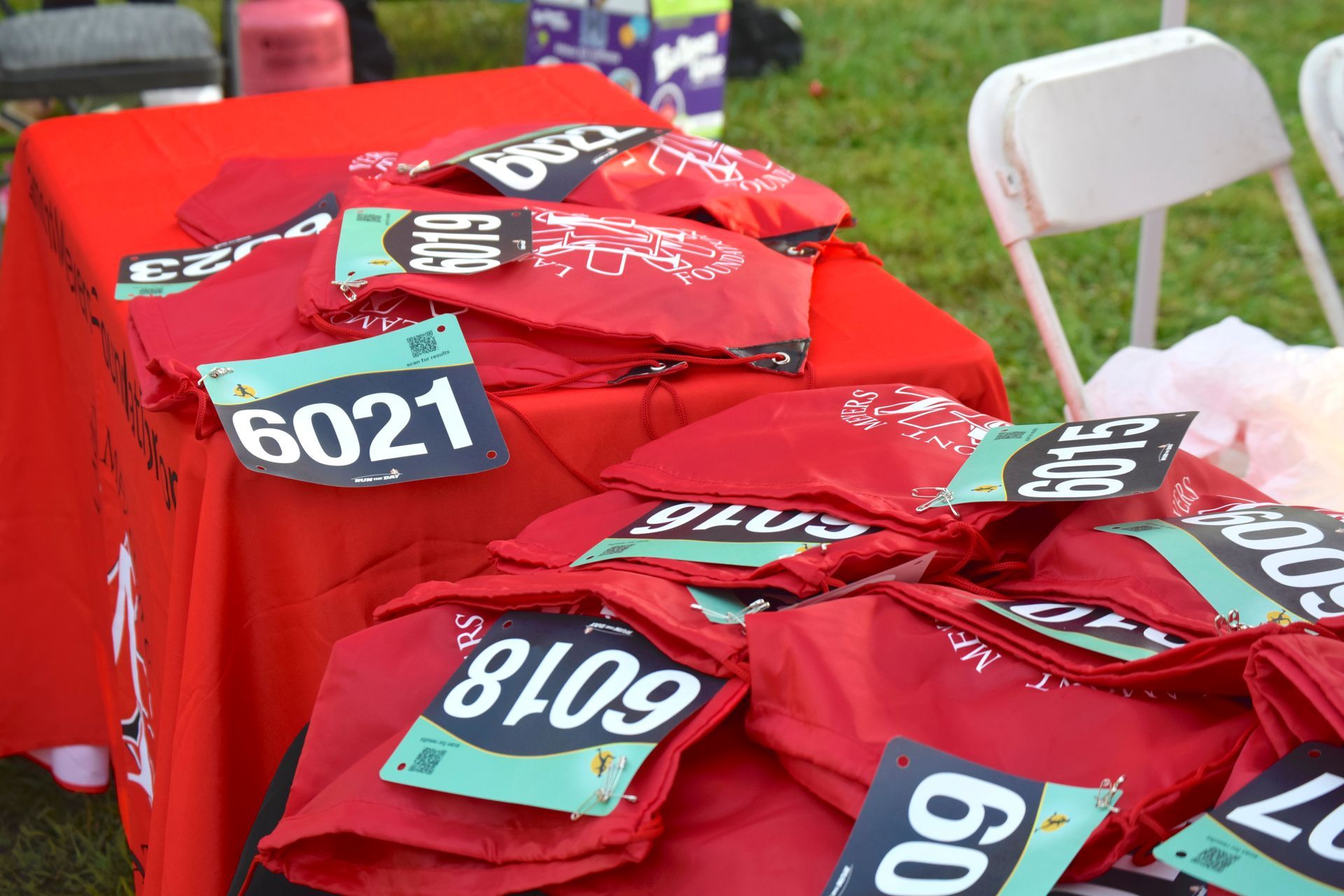 Red table with race bibs on it; outdoors. Bibs are black text on green or white.