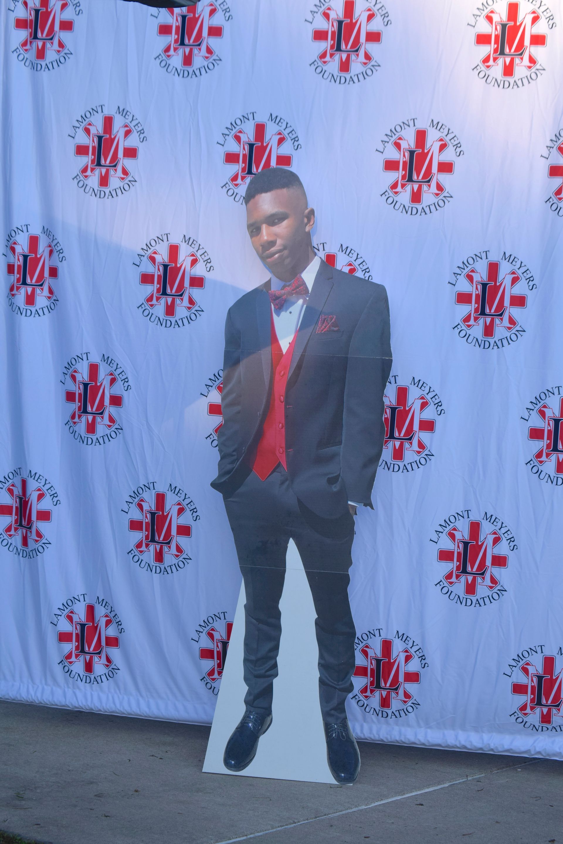 Cardboard cutout of a person in a suit, red vest and bow tie, standing in front of a patterned backdrop.
