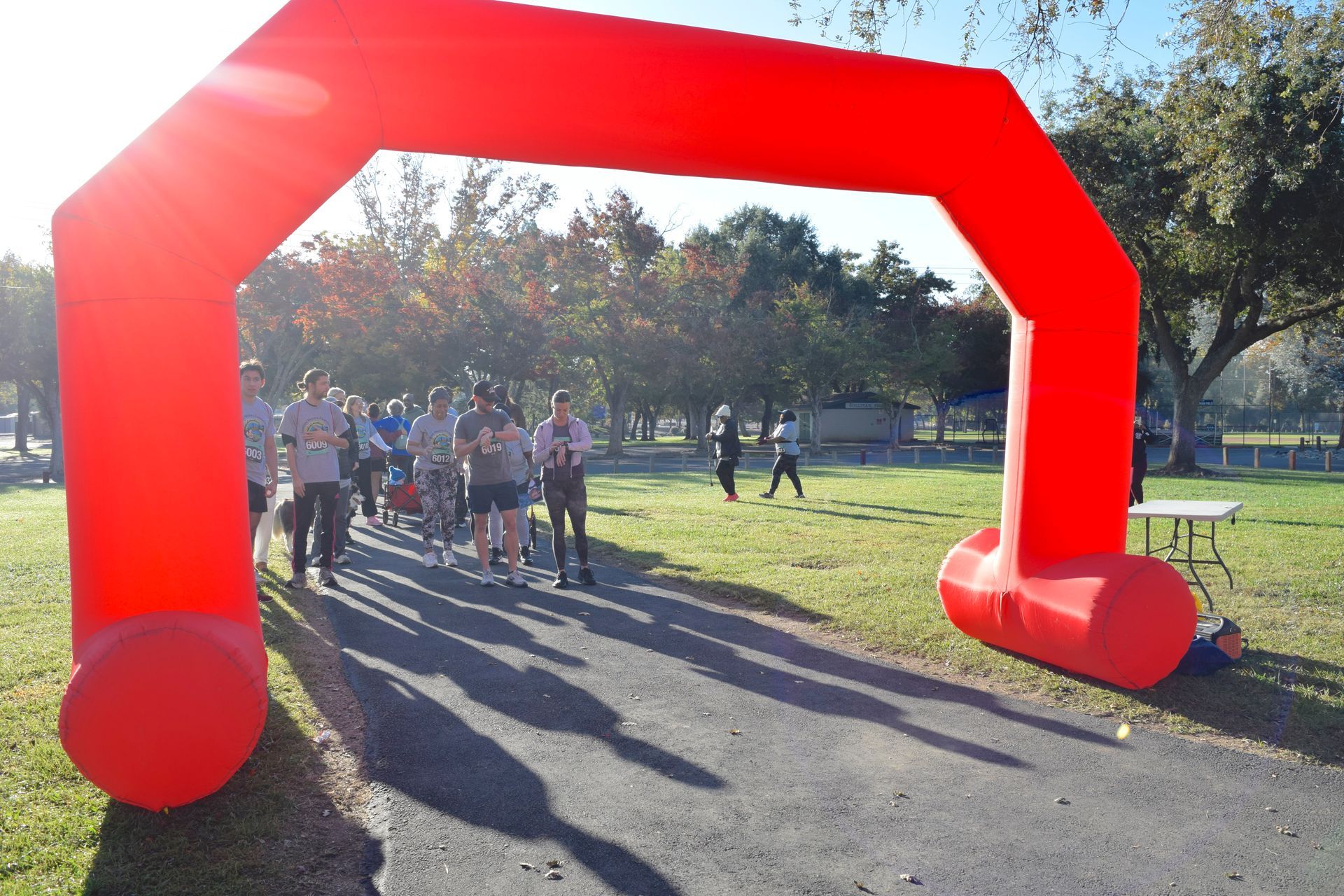 Red inflatable arch at a race start line; runners gather on a path in a park setting.