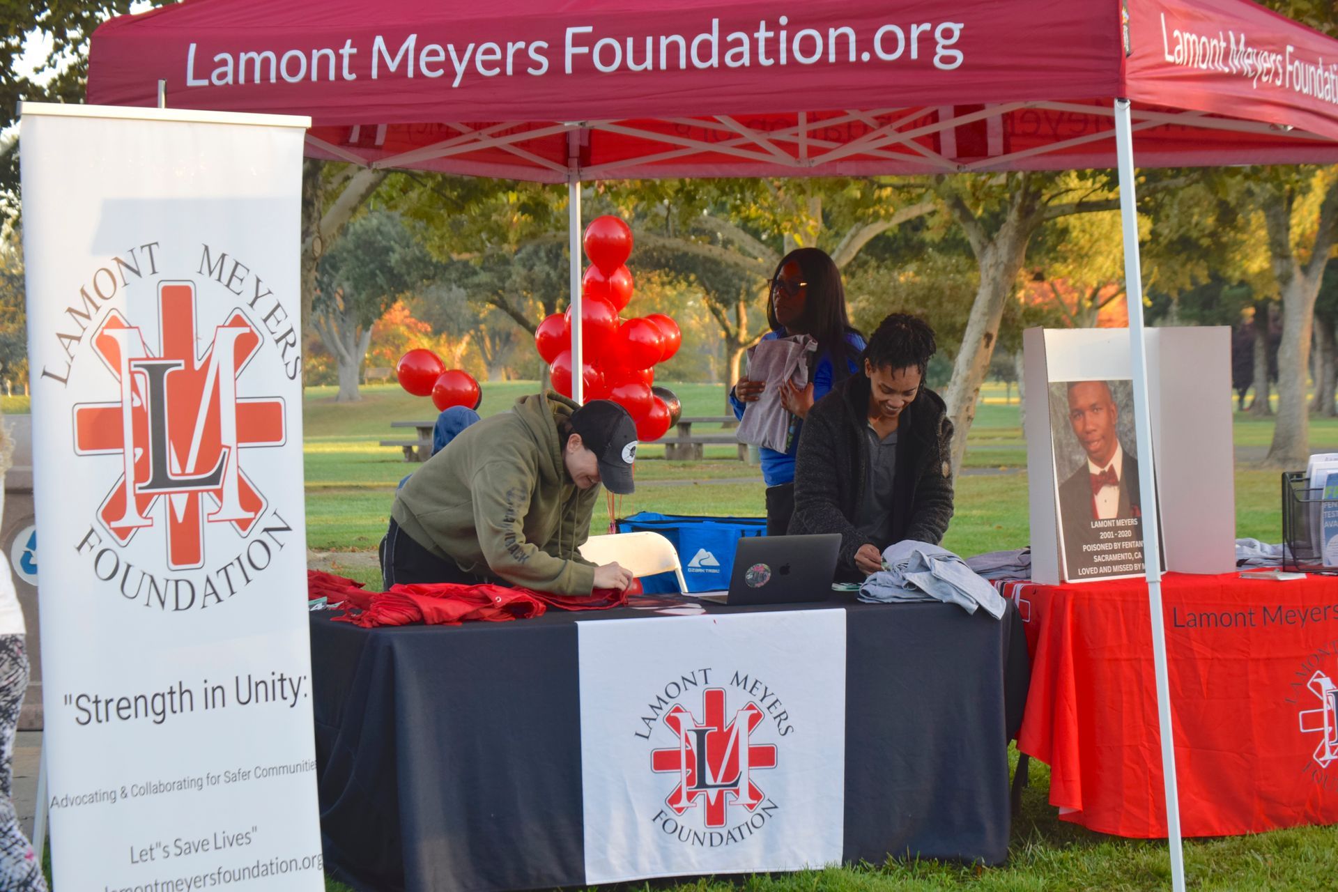 Lamont Meyers Foundation booth at an outdoor event, people at table with banner and red balloons.