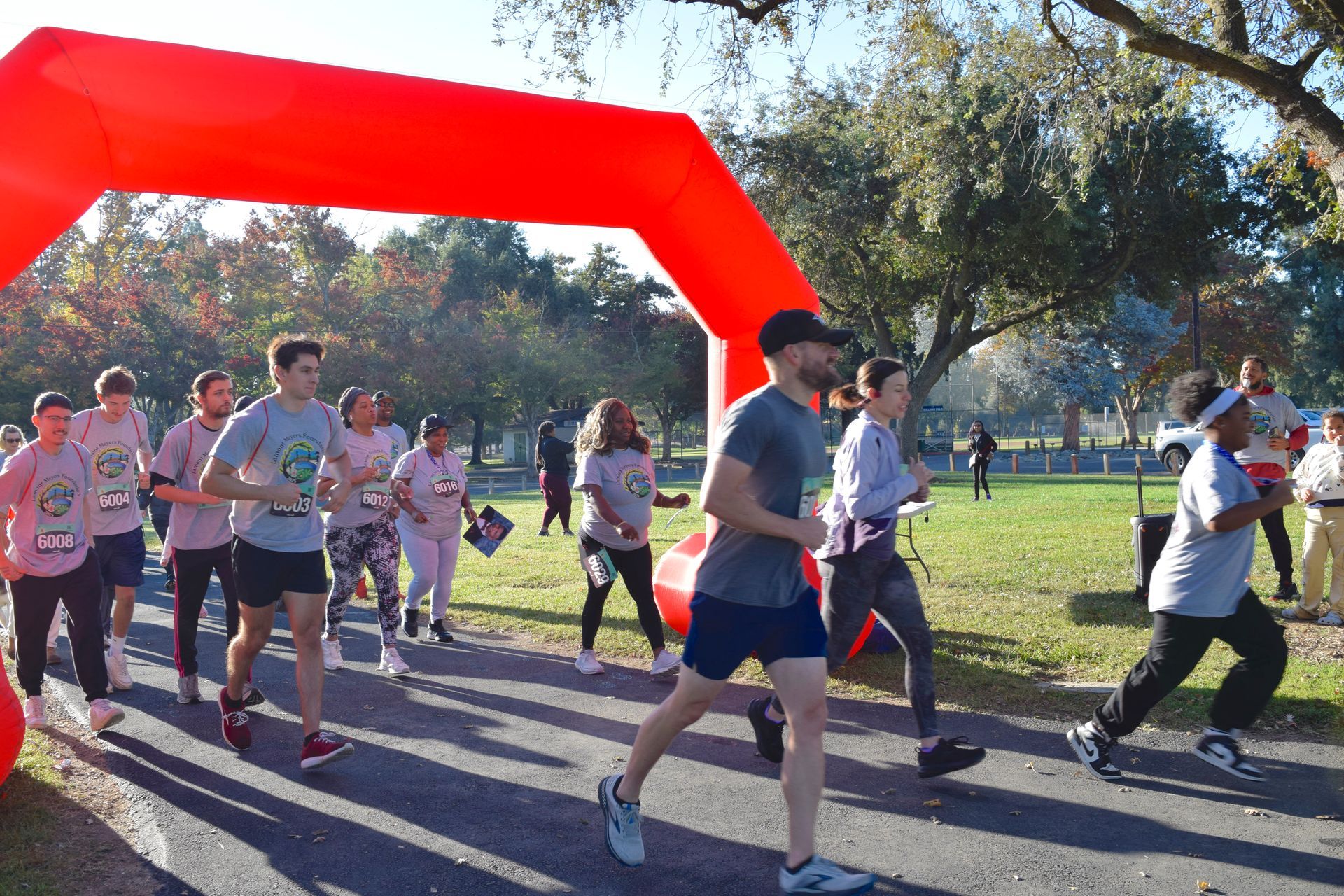 Runners exiting a red inflatable arch at a park race, sunny day.