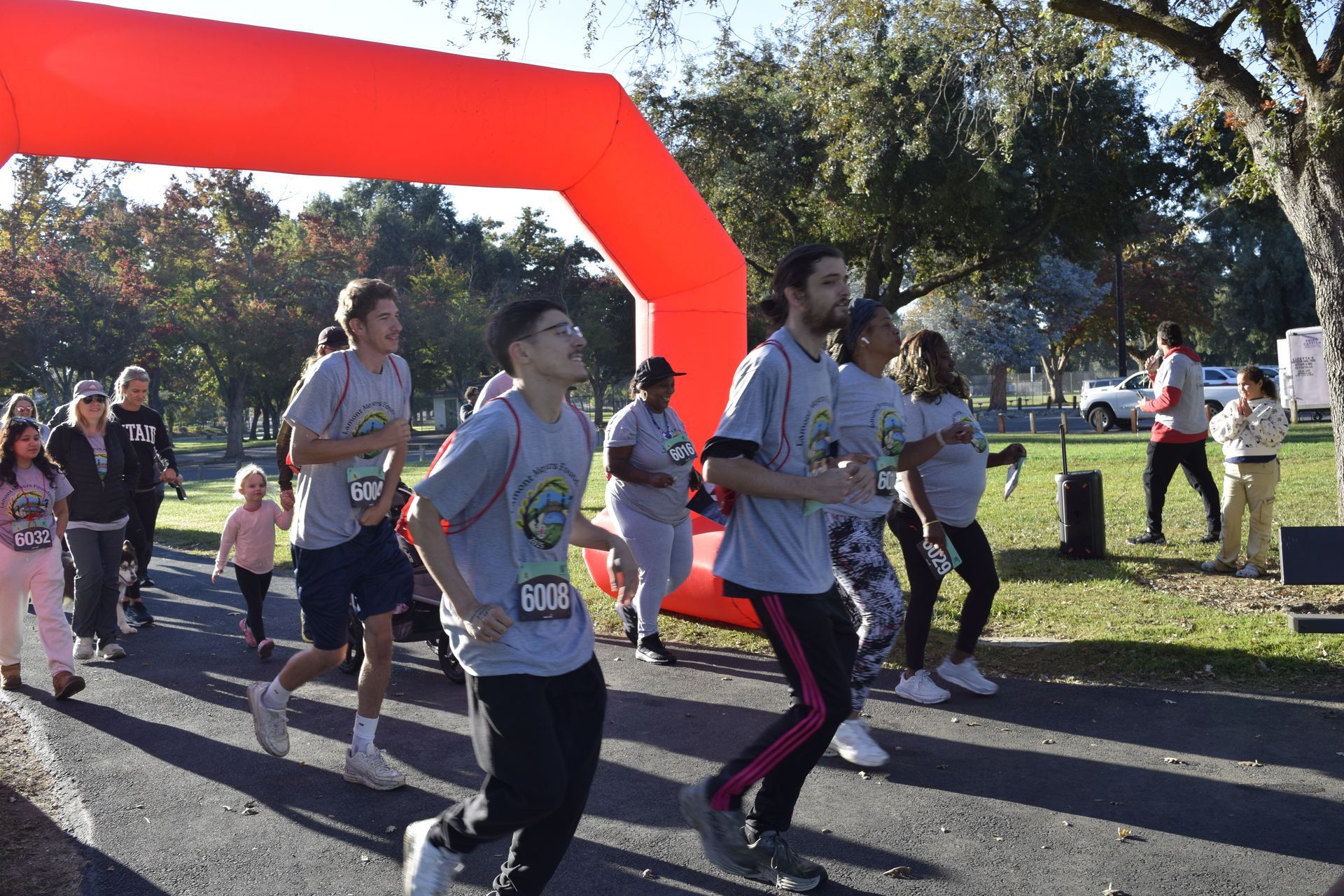Runners near an orange arch in a park, wearing gray shirts with logos.