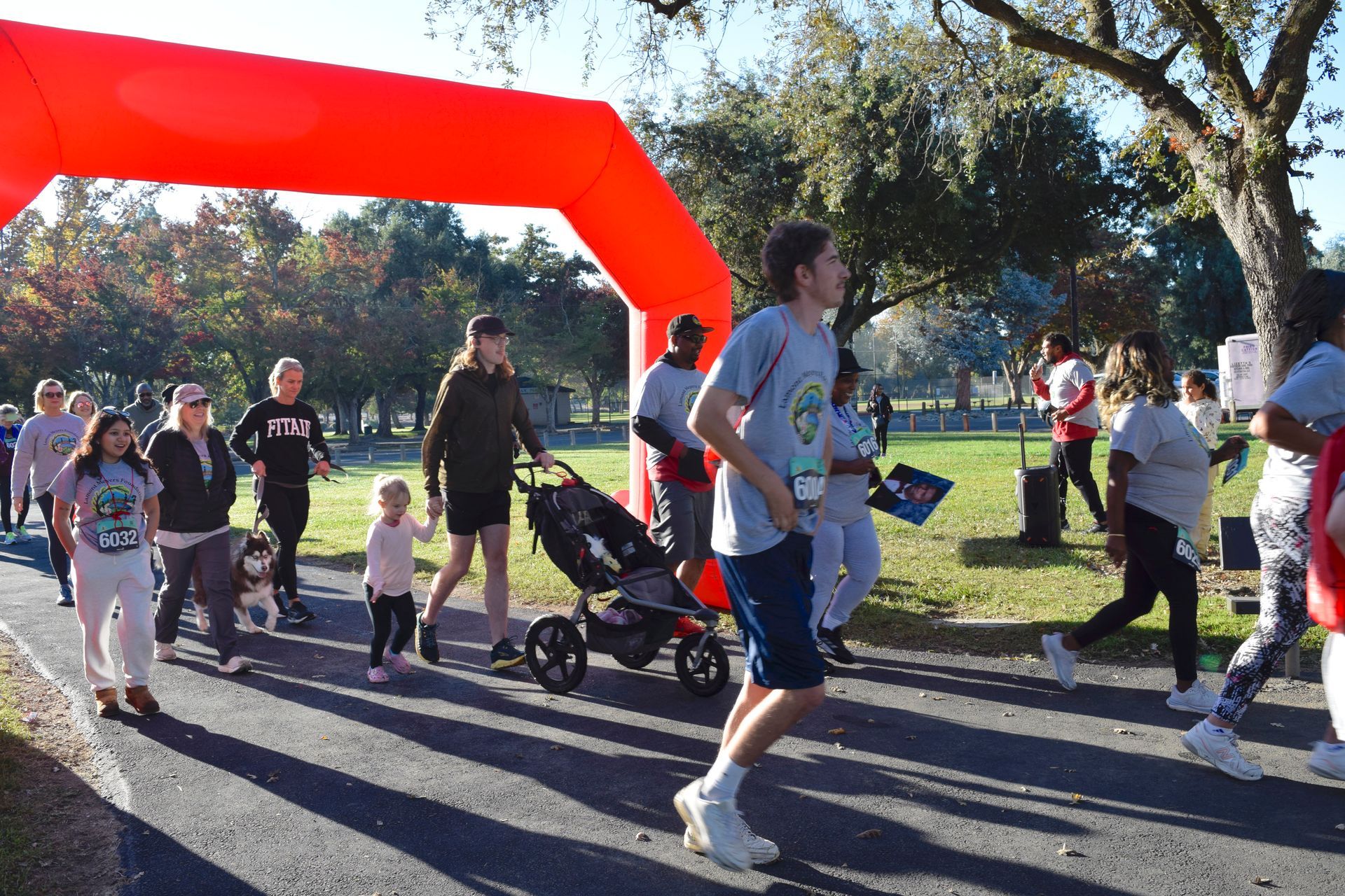 People walking/running under an orange arch at an outdoor event on a sunny day.