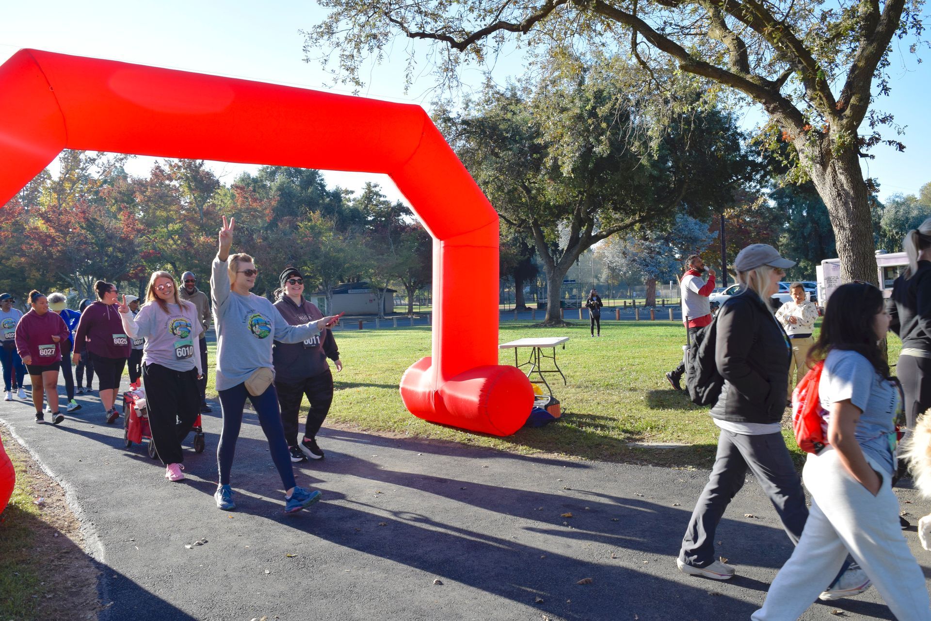 People walking under a red arch during an outdoor event. Others walking on the path nearby.