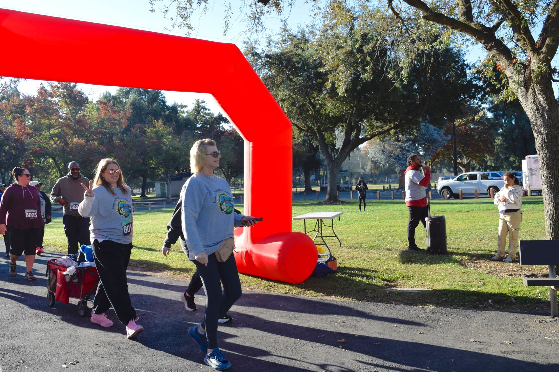 People walking under a red inflatable arch at an outdoor event, some carrying bags.