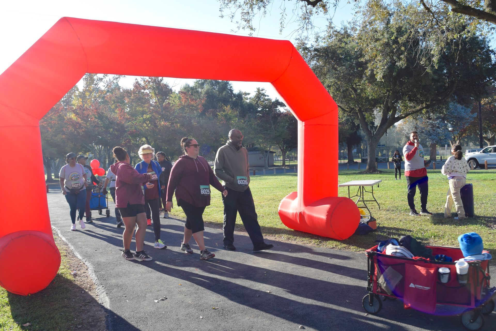People walking under a red archway at an outdoor event, with a park in the background.