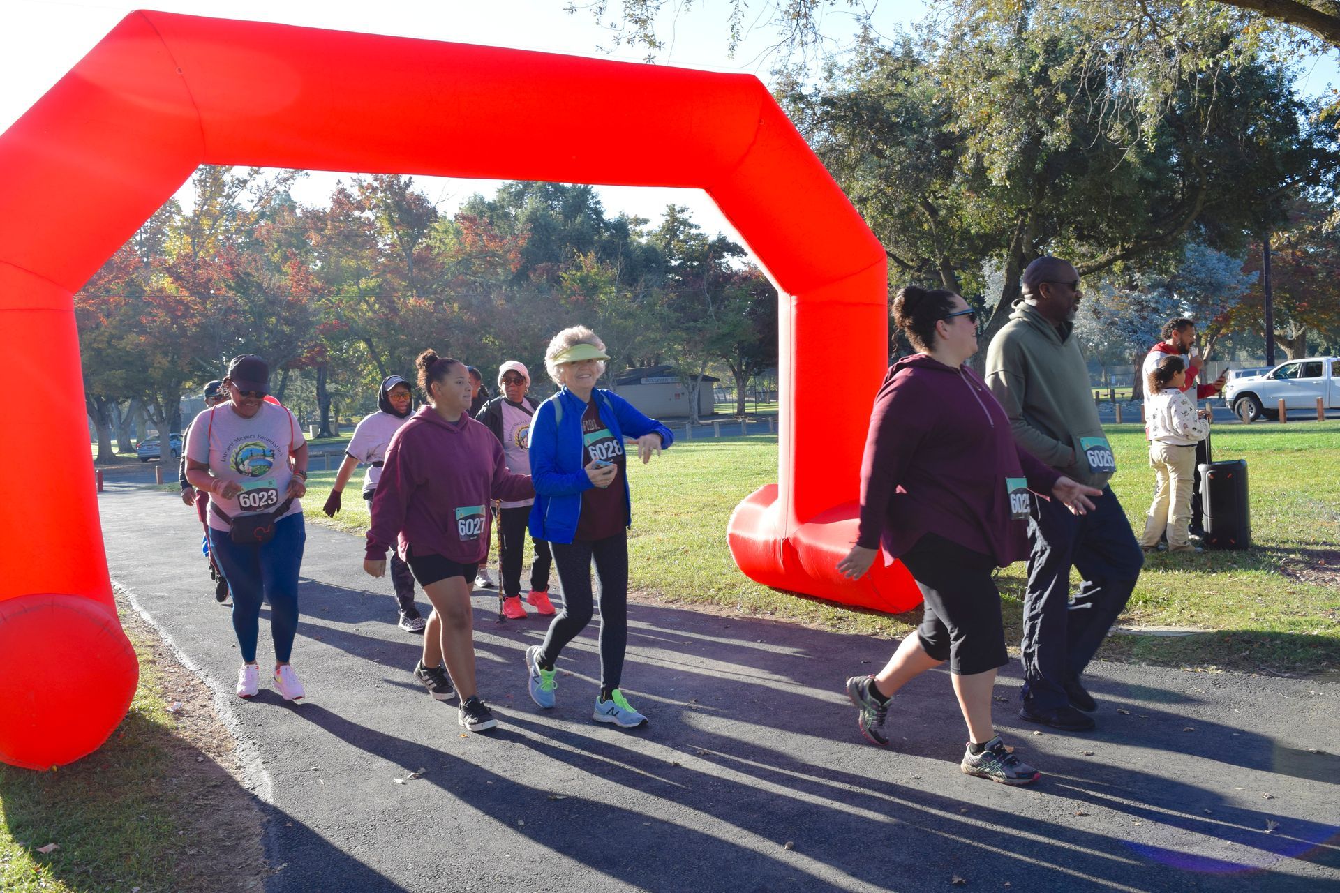 People walking under a red arch, likely at a race or event in a park.