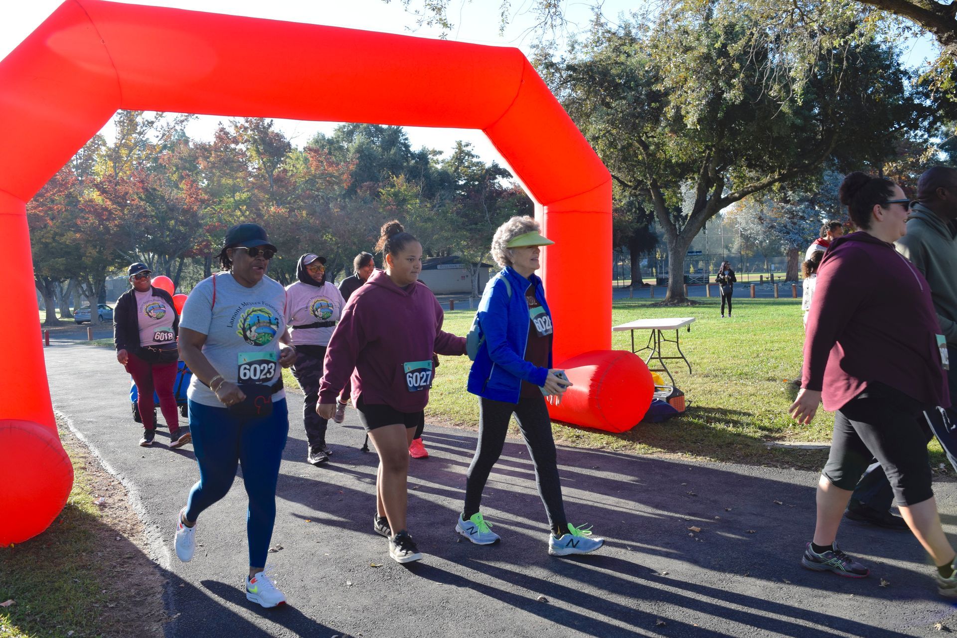 People walking under a red archway in a park, likely at the start or finish of a race or walk.