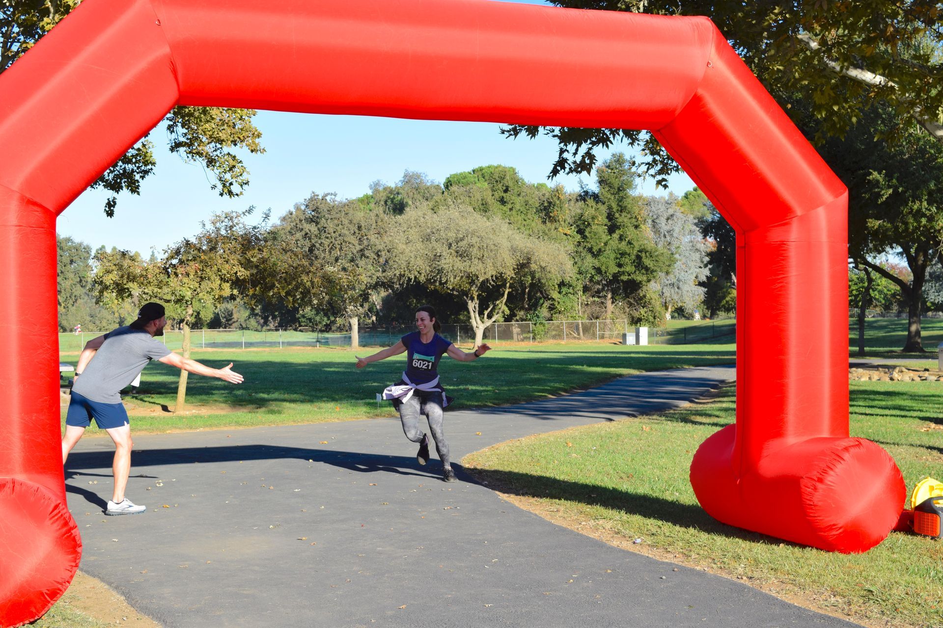 A runner crosses the finish line under a large red inflatable arch, cheered on by someone on the side.
