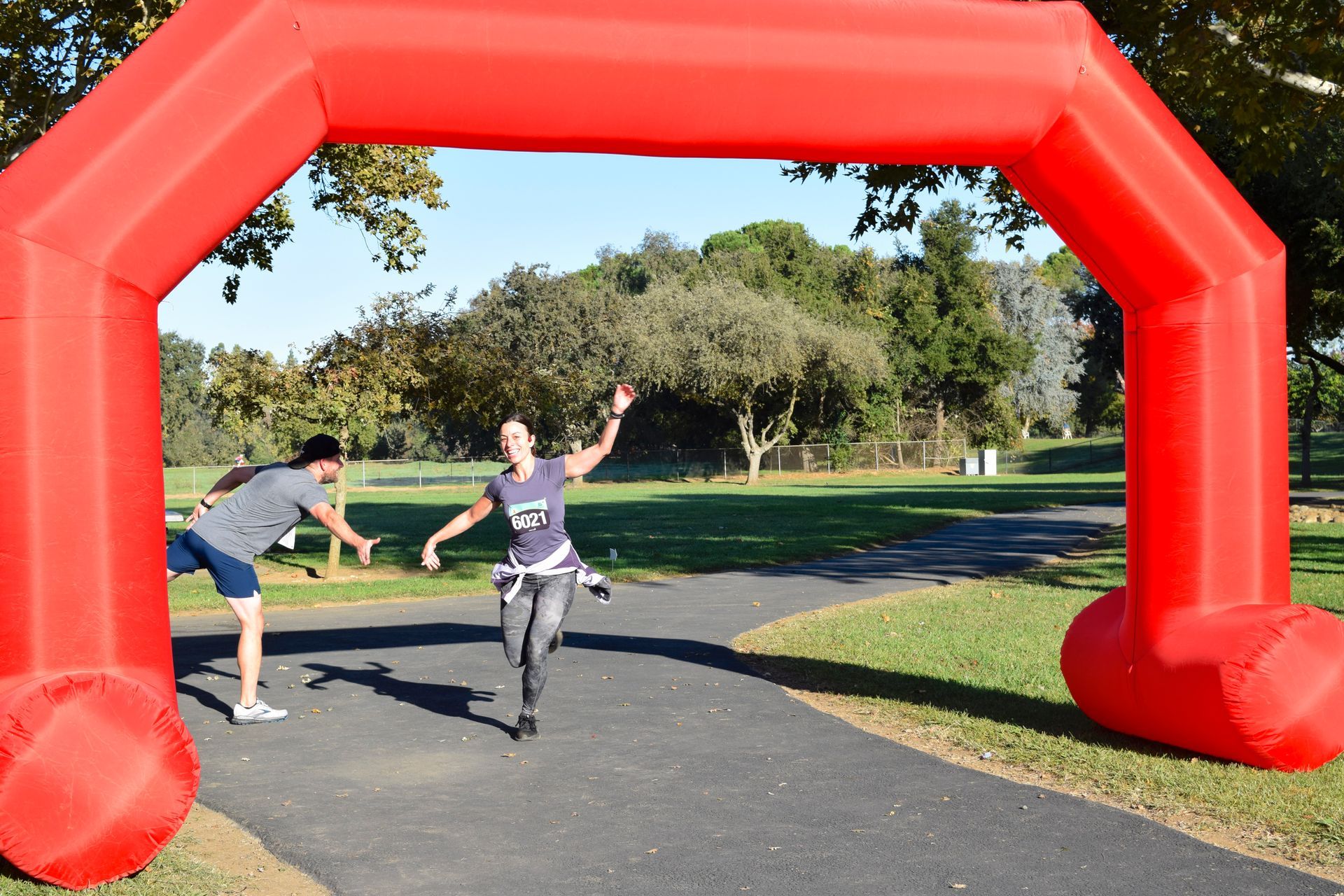 Runner crossing red inflatable arch finish line, arms raised in park.