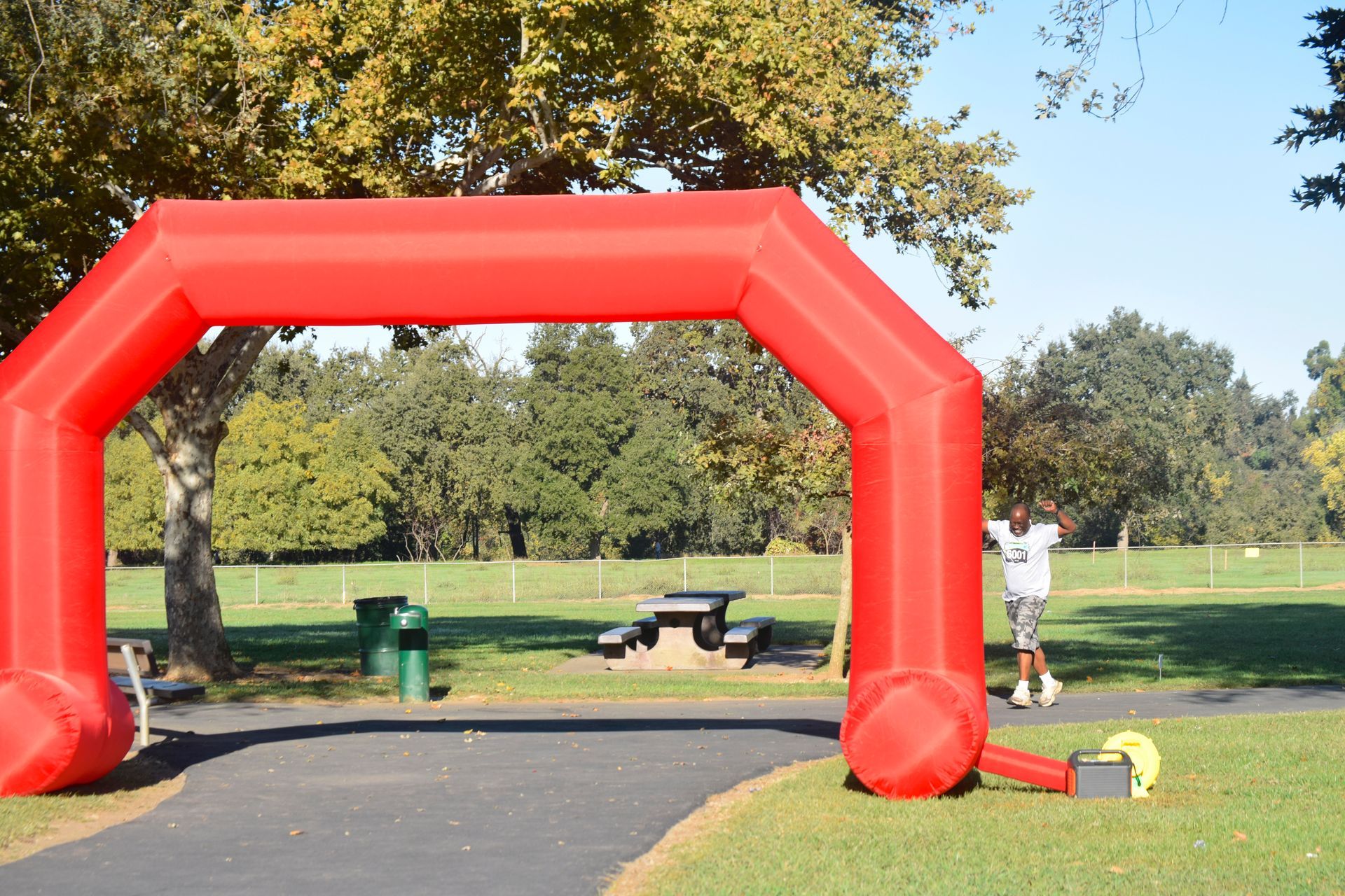 Red inflatable archway in a park; person runs toward it.