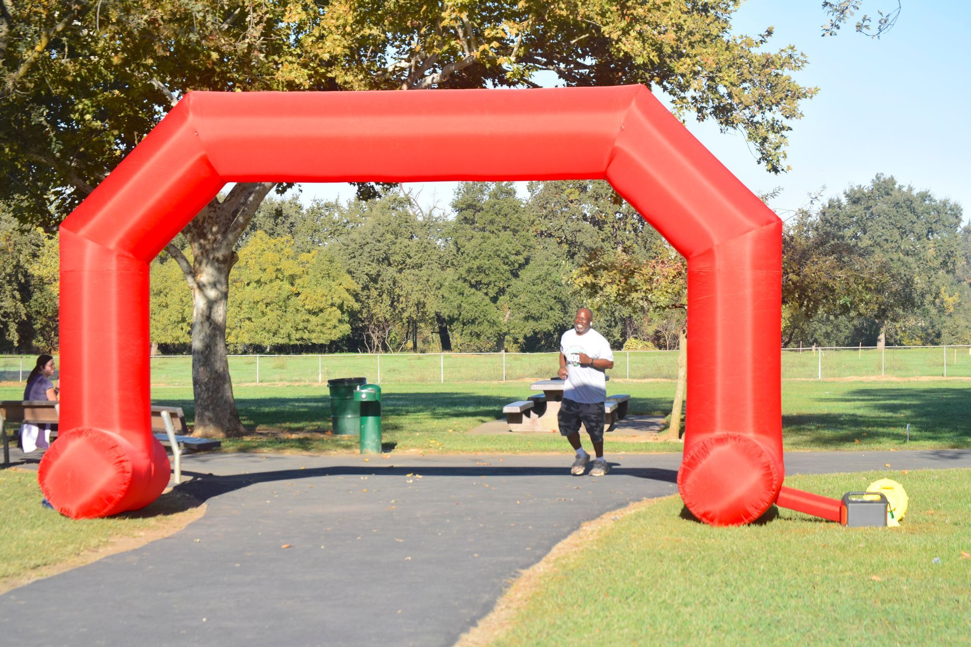 Red inflatable arch over a paved path in a park. A person runs towards the arch.