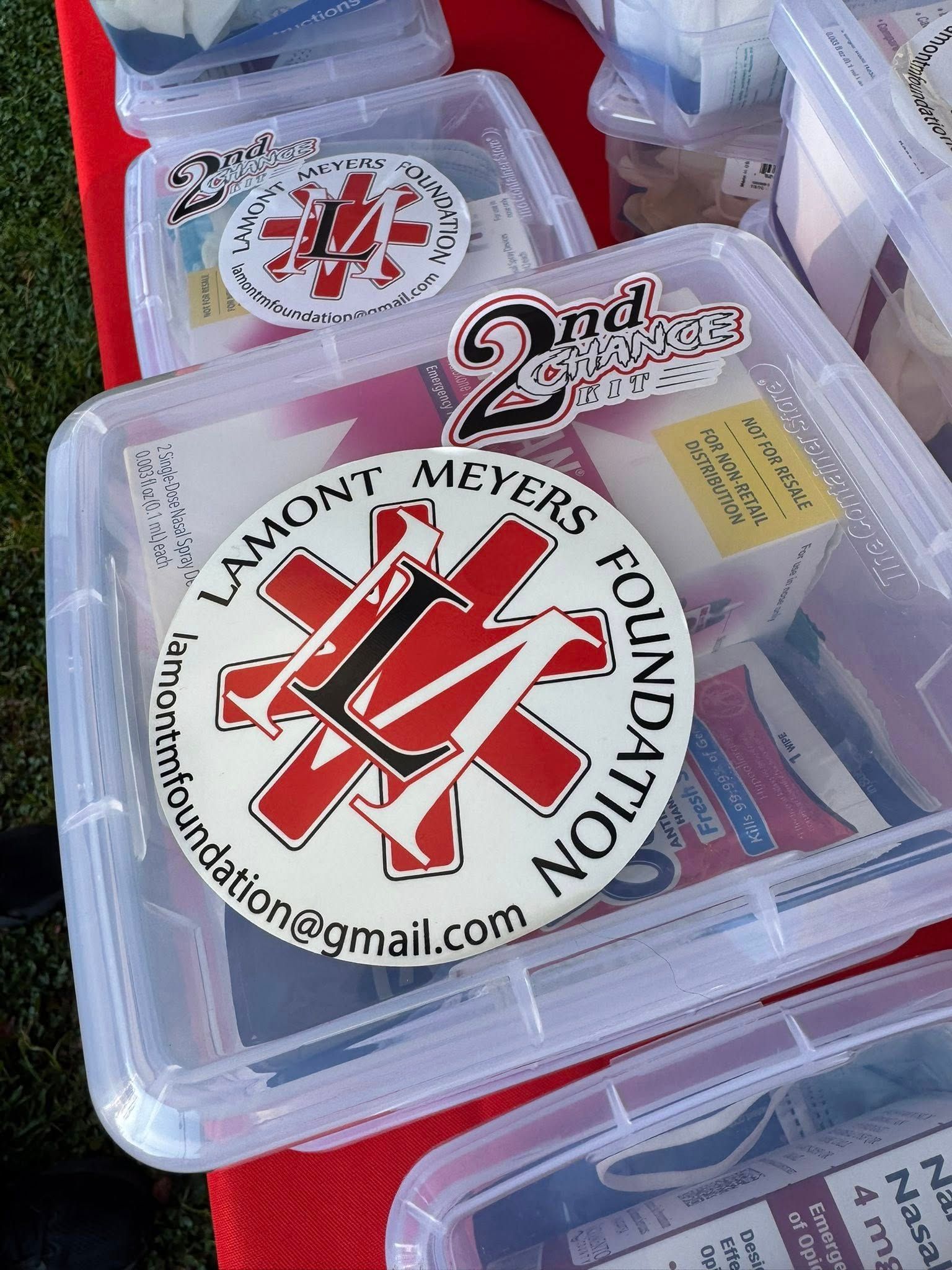 Clear plastic containers with Lamont Meyers Foundation stickers on a red surface.