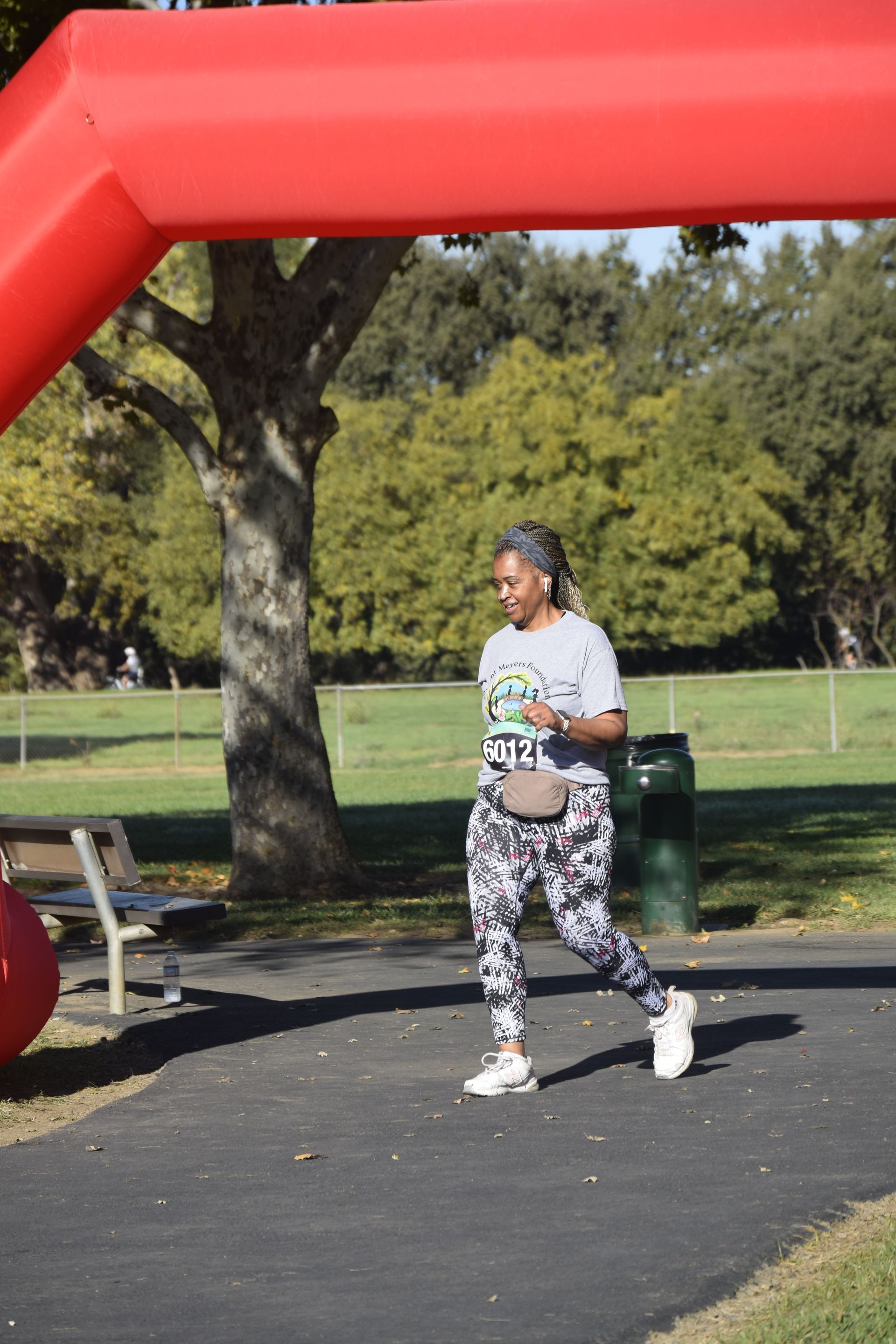 Woman in athletic wear walks under a red arch in a park, smiling.