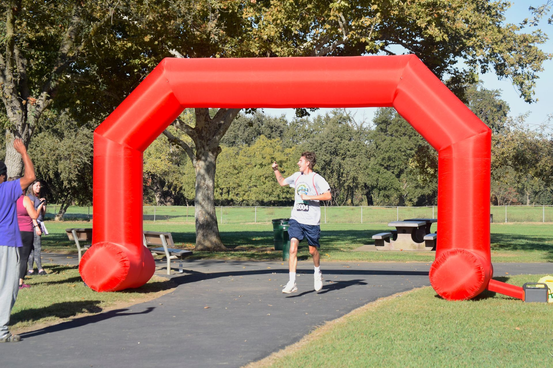 Runner crossing finish line under a large red inflatable arch in a park.