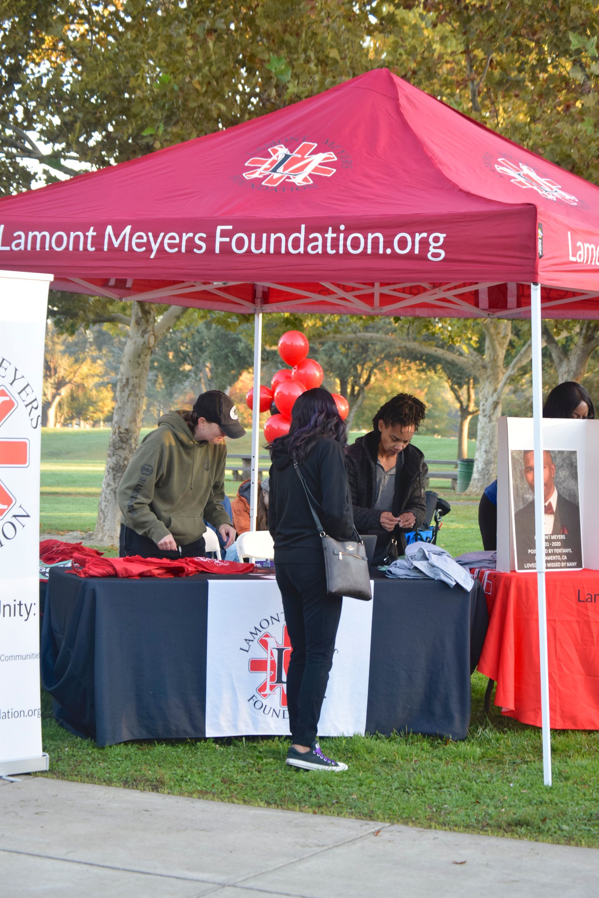Lamont Meyers Foundation booth at outdoor event with people. A red tent has the organization's logo.