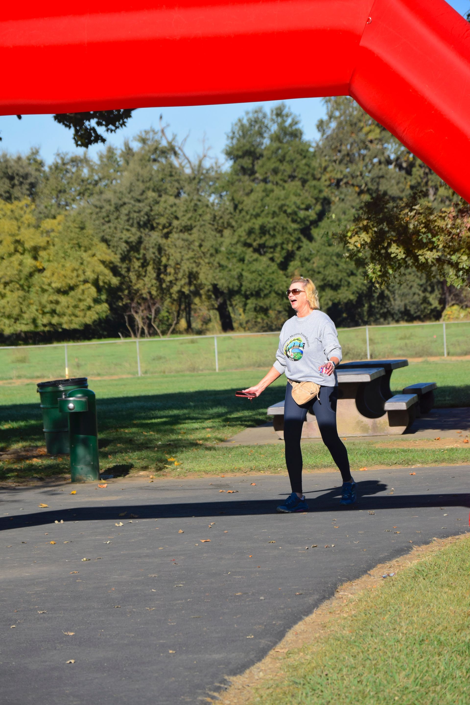 Woman in a sweatshirt running under a red archway in a park.