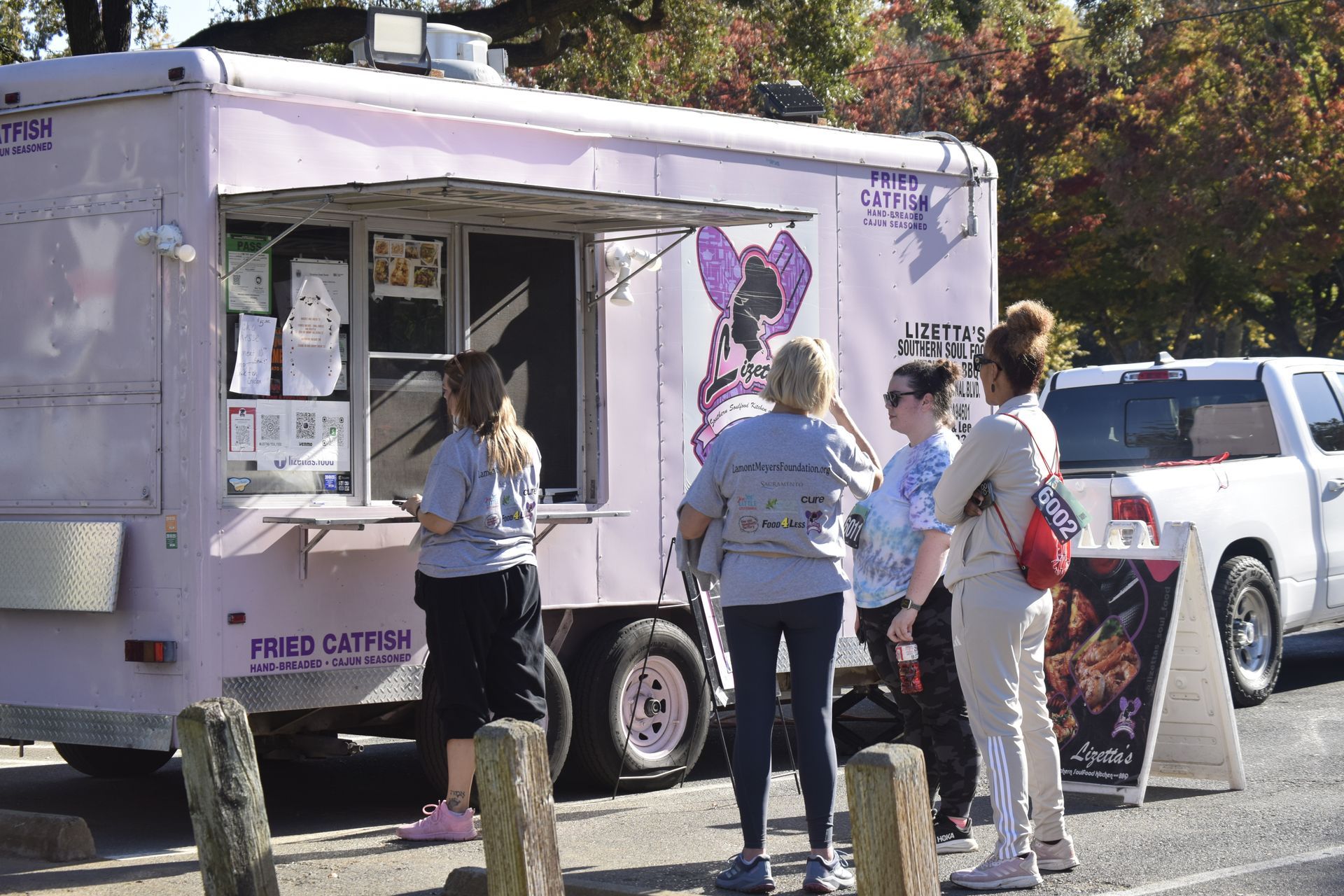 A pink food truck with customers waiting in line. The truck has a cartoon cat logo.
