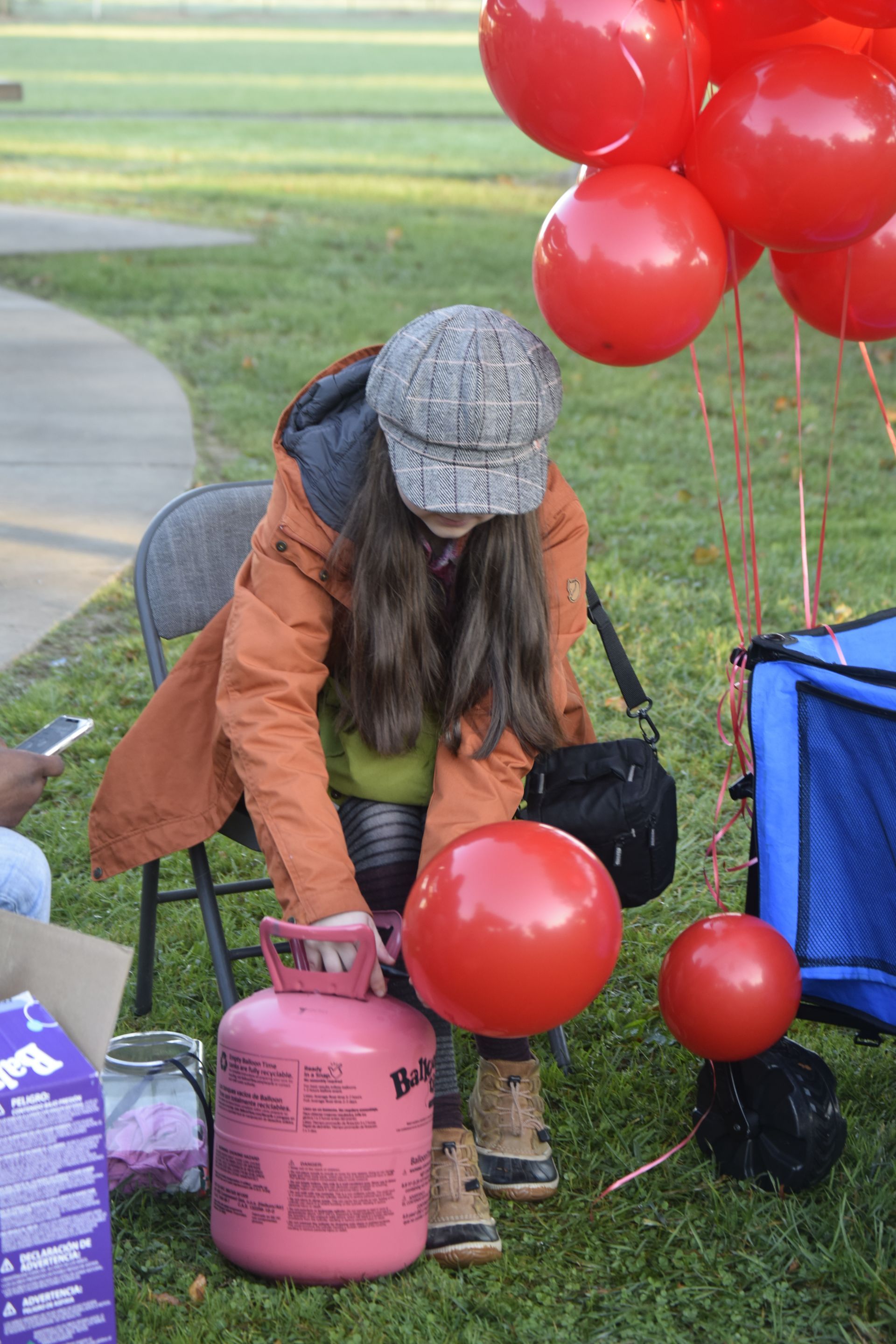 Person inflating a red balloon with a pink helium tank outside. Several other red balloons are nearby.