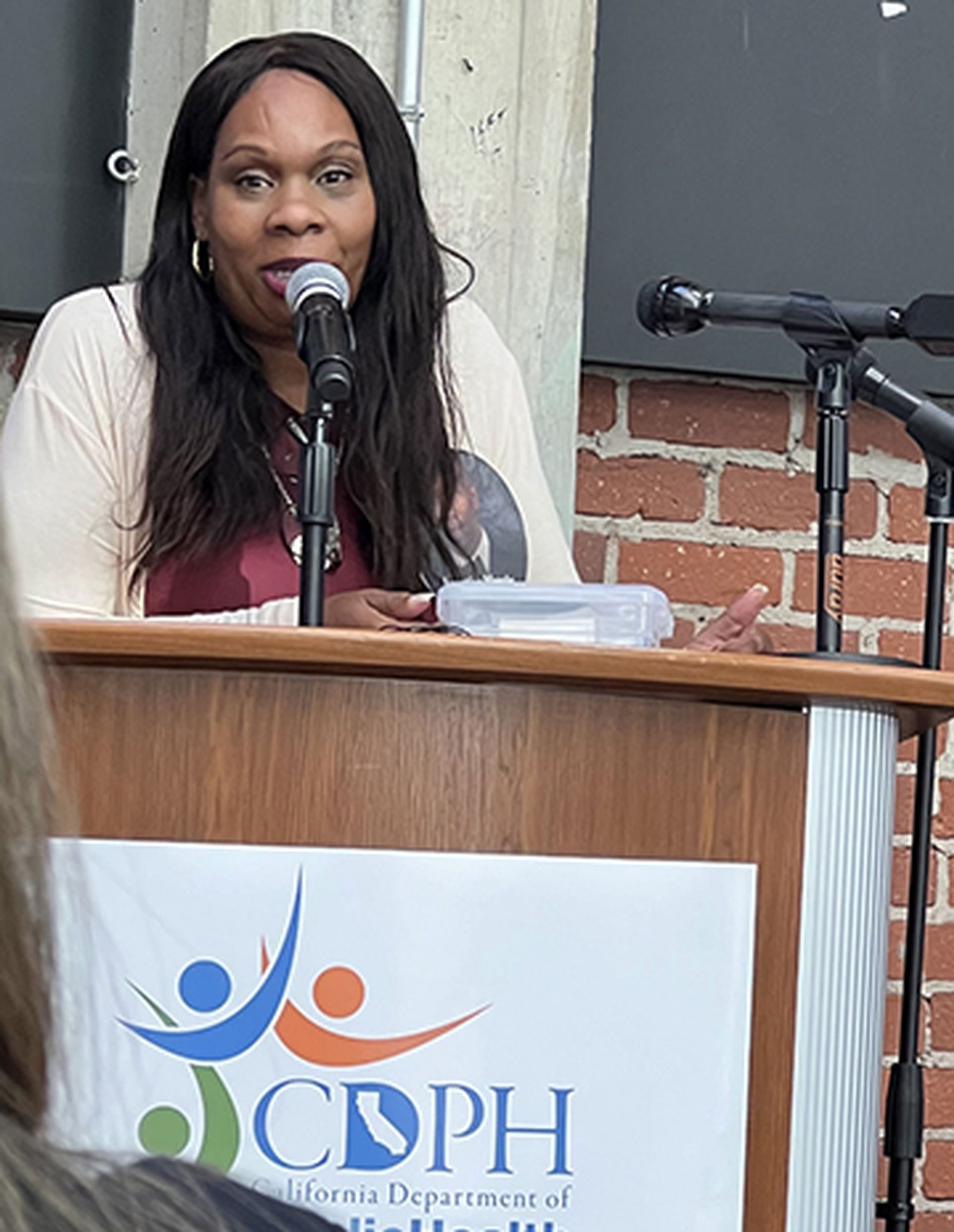 A woman is speaking into a microphone at a podium that says cdph