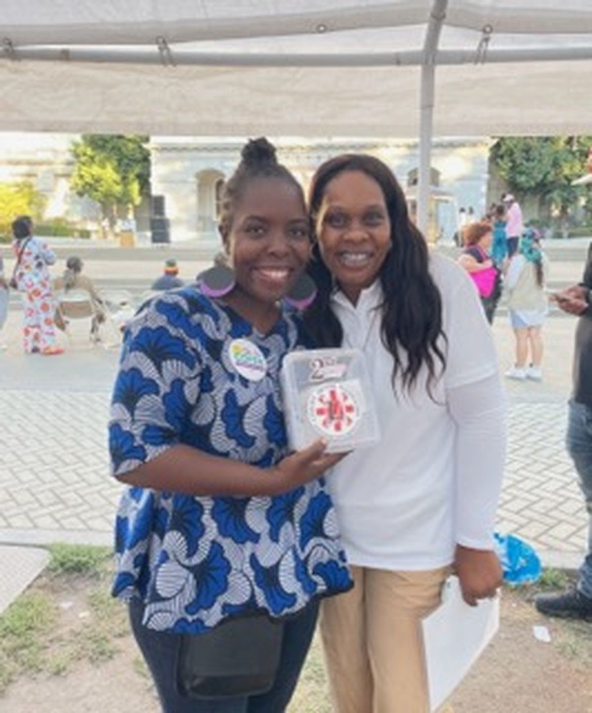 Two women are posing for a picture and one is holding a box with a red cross on it
