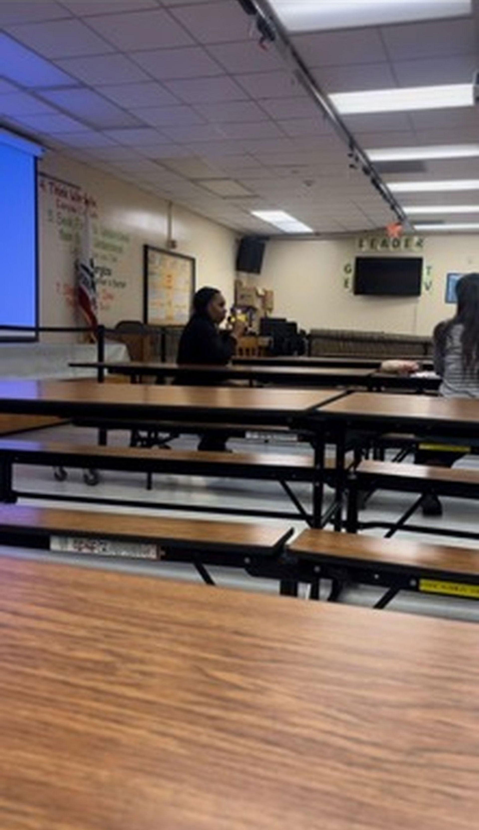 A classroom with tables and benches and a projector screen