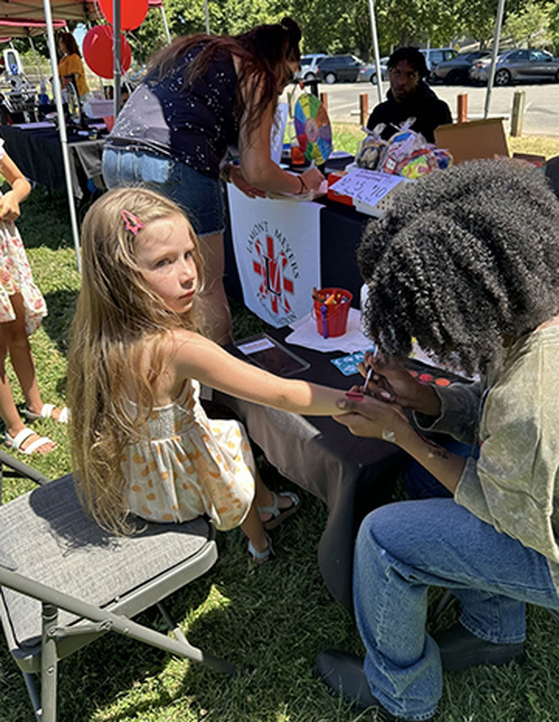 A little girl is getting her hands painted at a table.