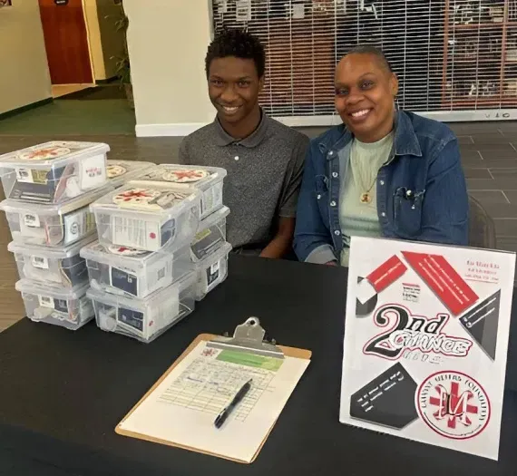 Two people are sitting at a table with a sign that says 2nd grade