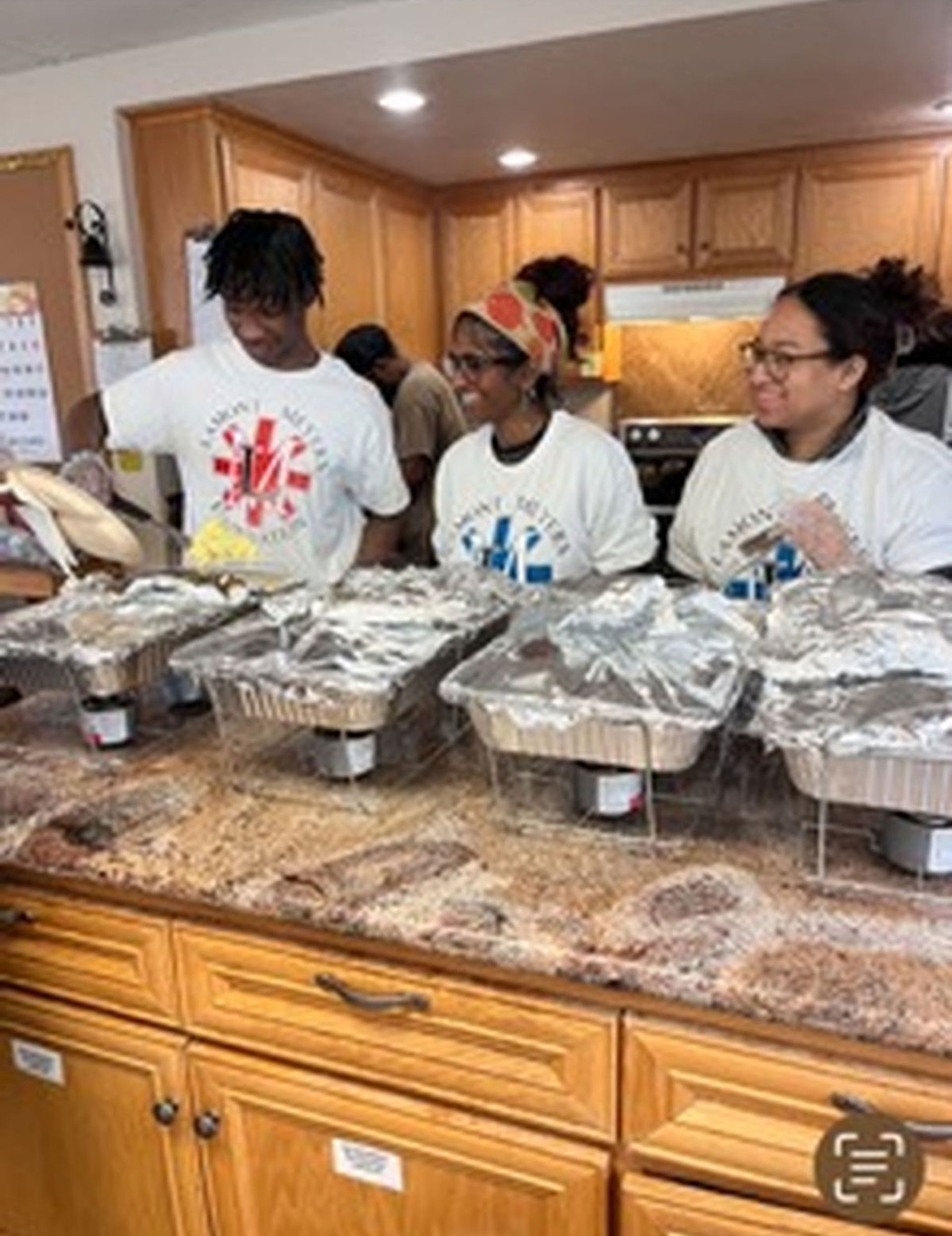 People preparing food in a kitchen; chafing dishes on counter.