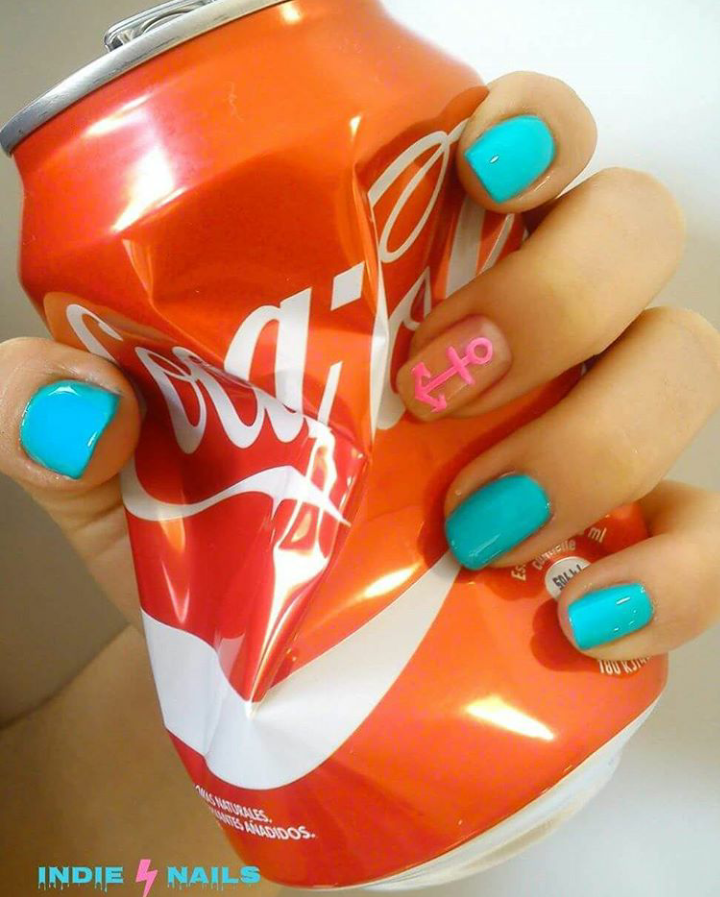 Una mujer con uñas azules sostiene una lata de Coca Cola aplastada.