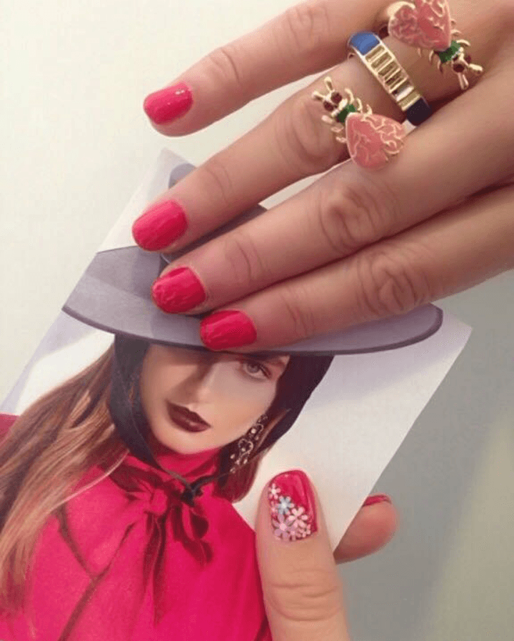 Una mujer con uñas rojas sostiene una foto de una mujer con sombrero.