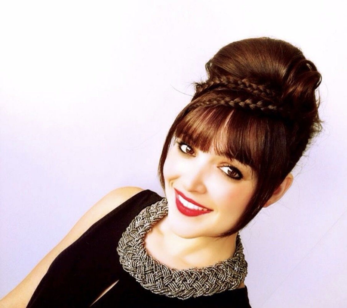 Una mujer que lleva un moño trenzado y un collar sonríe para la cámara.