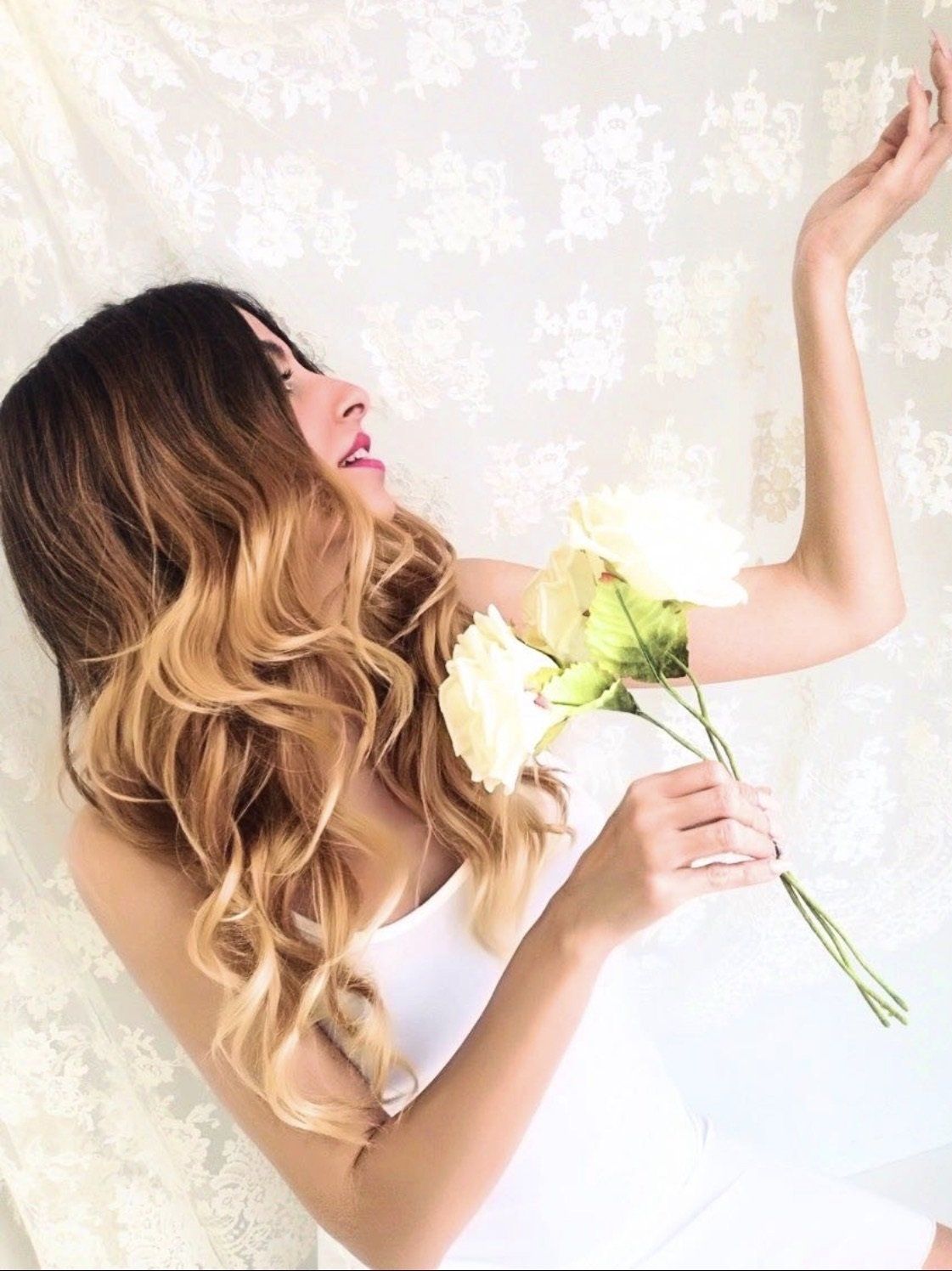 Una mujer con un vestido blanco sostiene una rosa blanca.