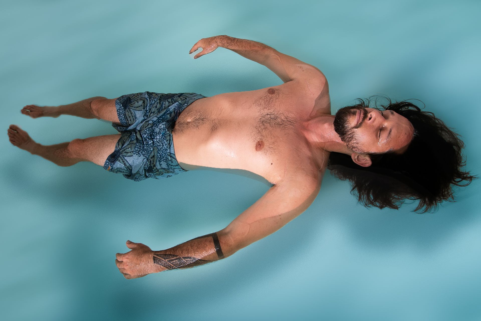 A shirtless man is floating on his back in a pool.