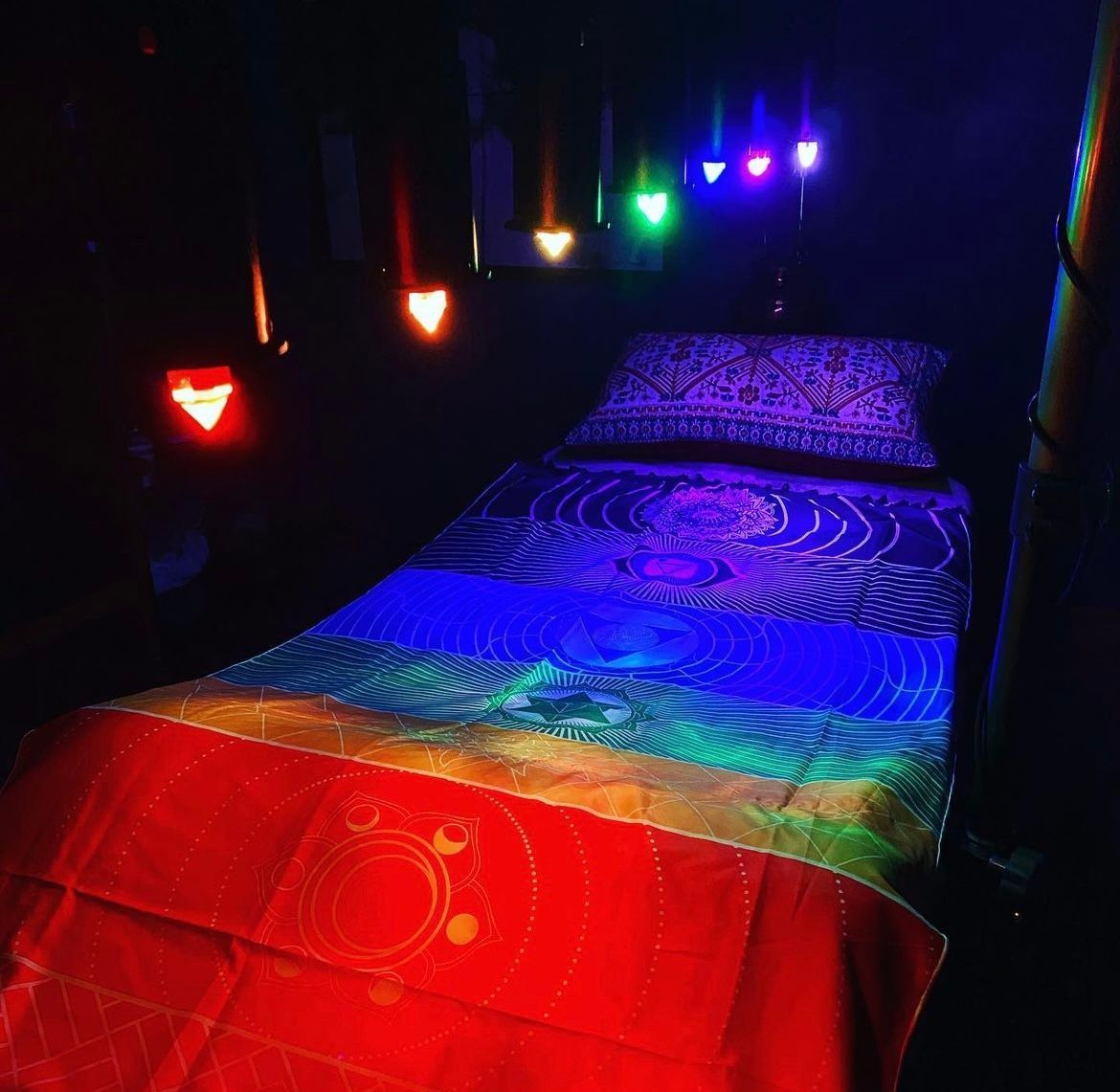 A bed with a rainbow colored blanket and pillows in a dark room.