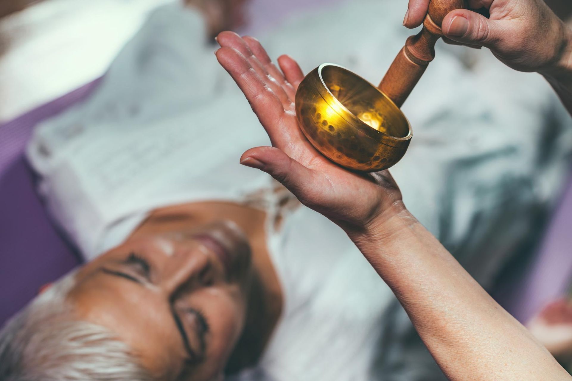 A person is holding a bowl in their hand while a man is laying on a bed.